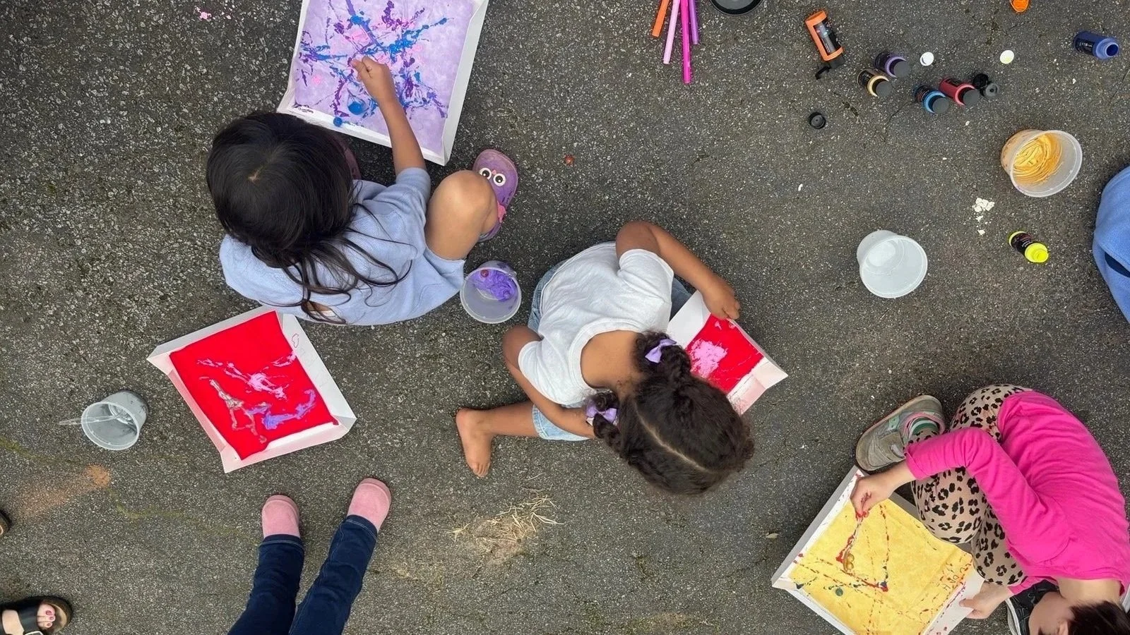 Jewish children sit together on the ground and create colorful matzah covers by painting with marbles.