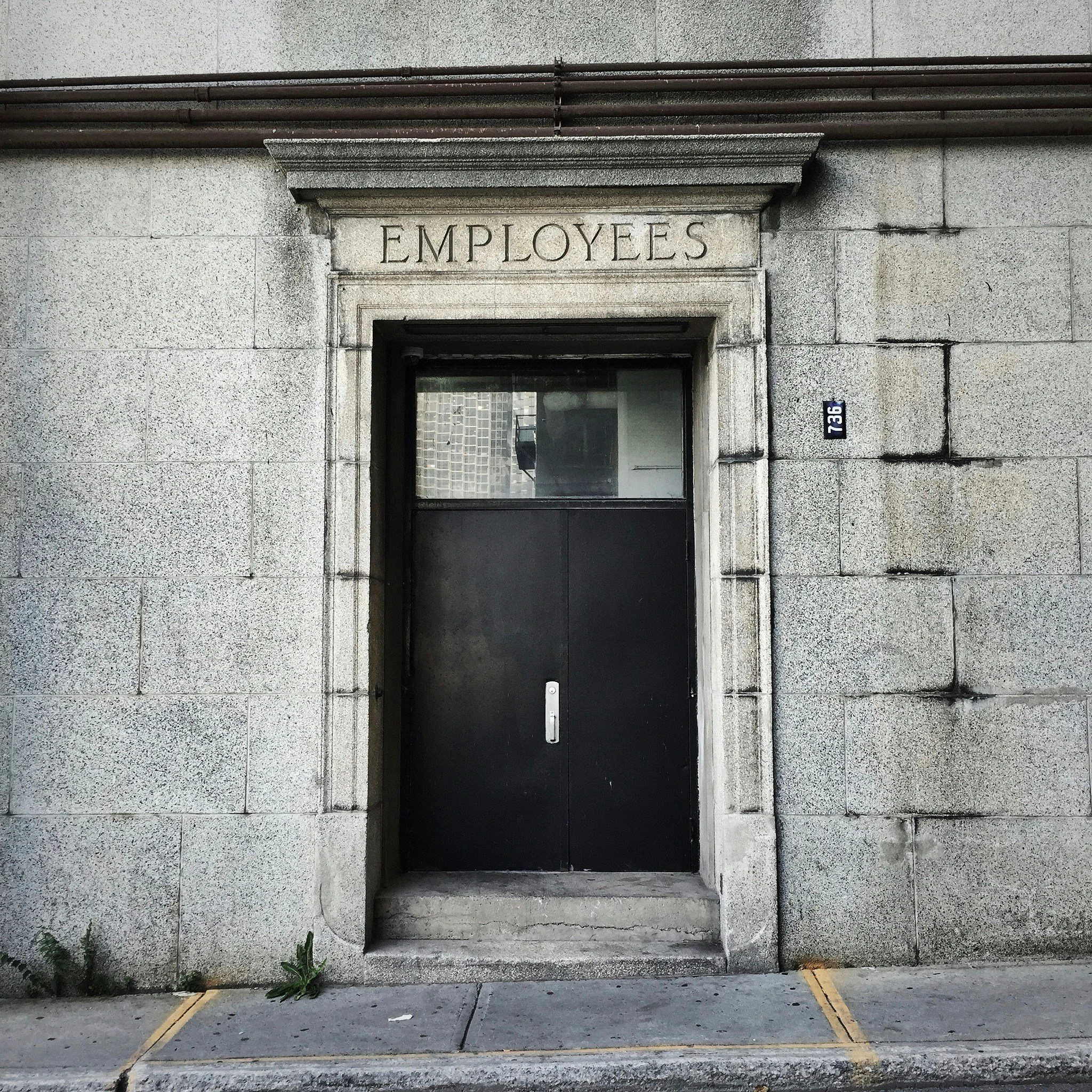Entrance with a sign that reads 'Employees' above the door, made of stone or concrete, with the building number 1736 on a plaque to the right.