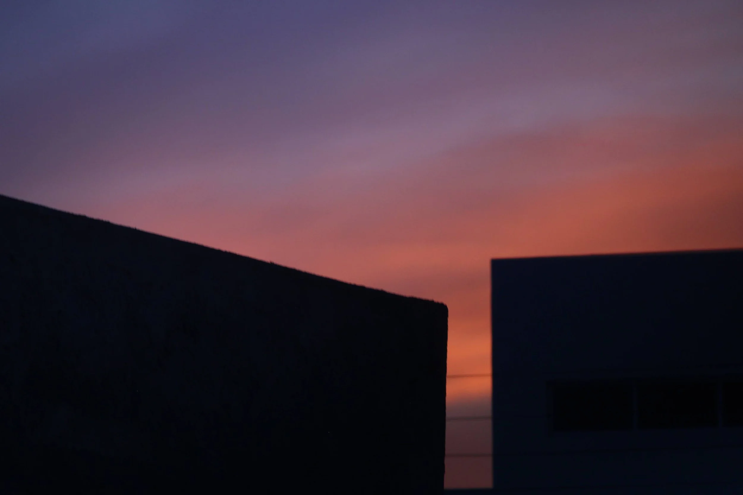 Silhouetted rooftops against a colorful sunset sky with shades of purple, pink, and orange.
