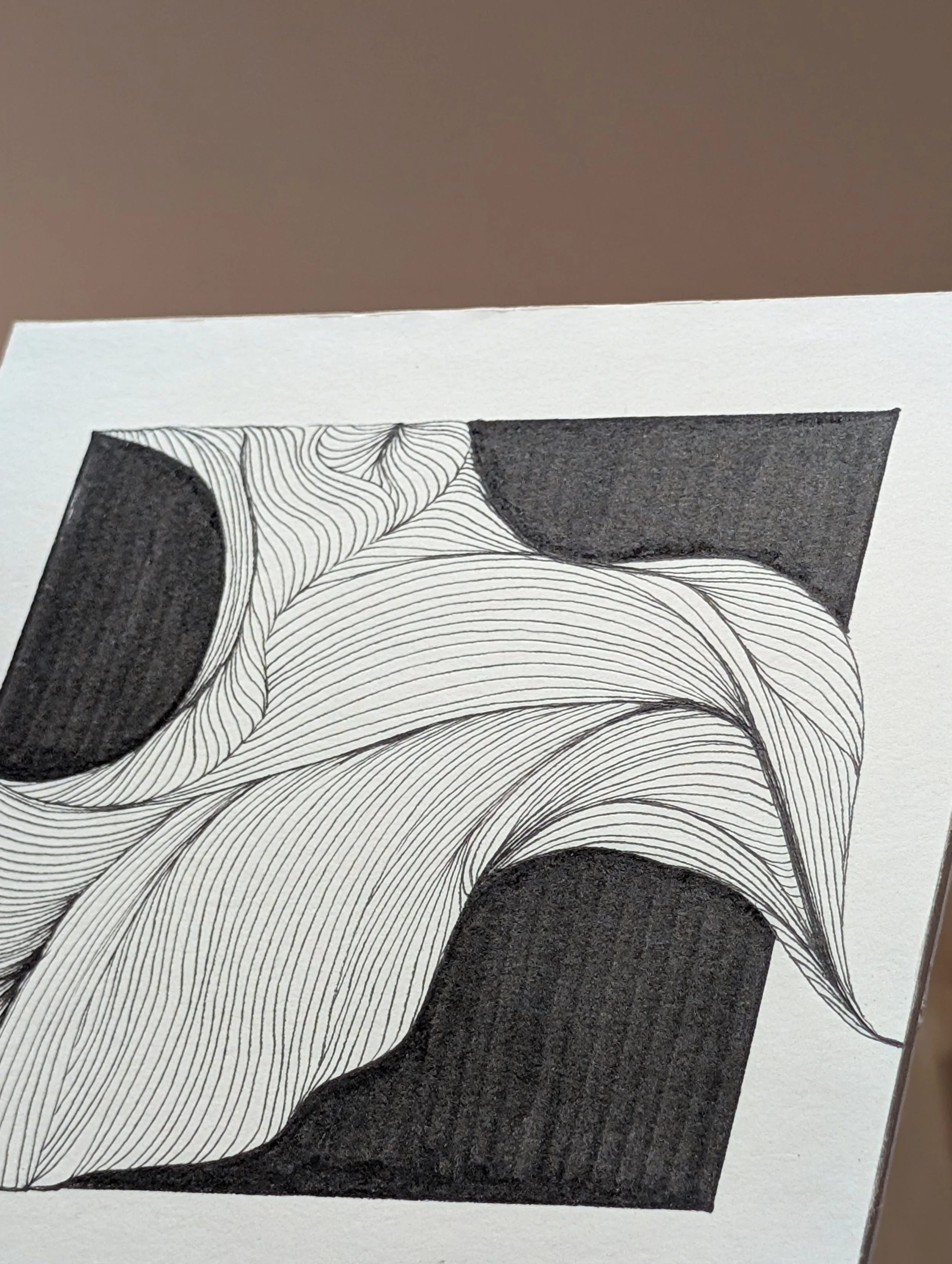 A black and white piece of abstract art with curving lines and large black shapes on white paper, laid on a flat surface.