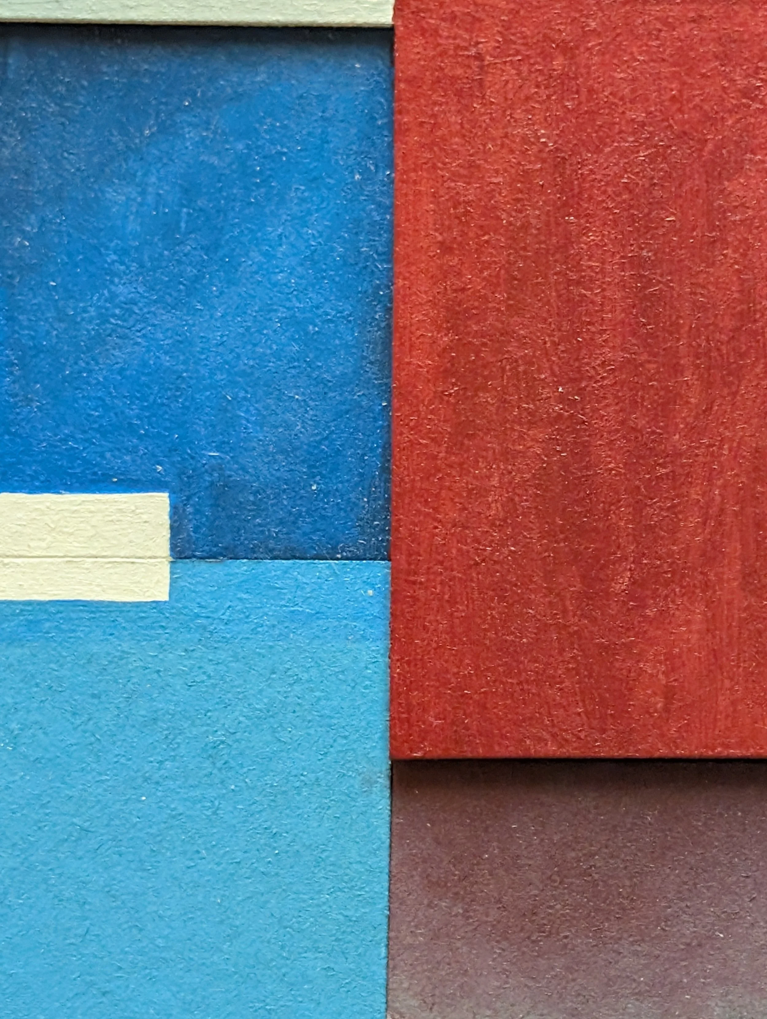Close-up of a textured wall with large blocks painted in red, blue, cream, and gray.