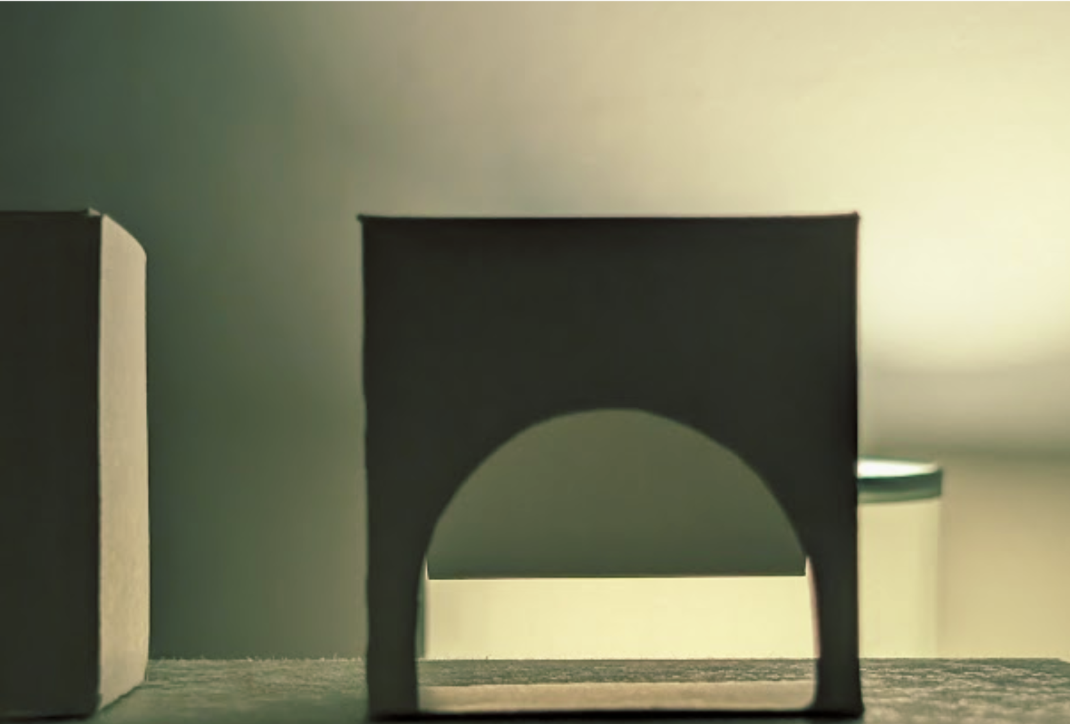 Close-up of a black cardboard object with a semi-circular cutout at the bottom, placed on a wooden surface near a light-colored wall.