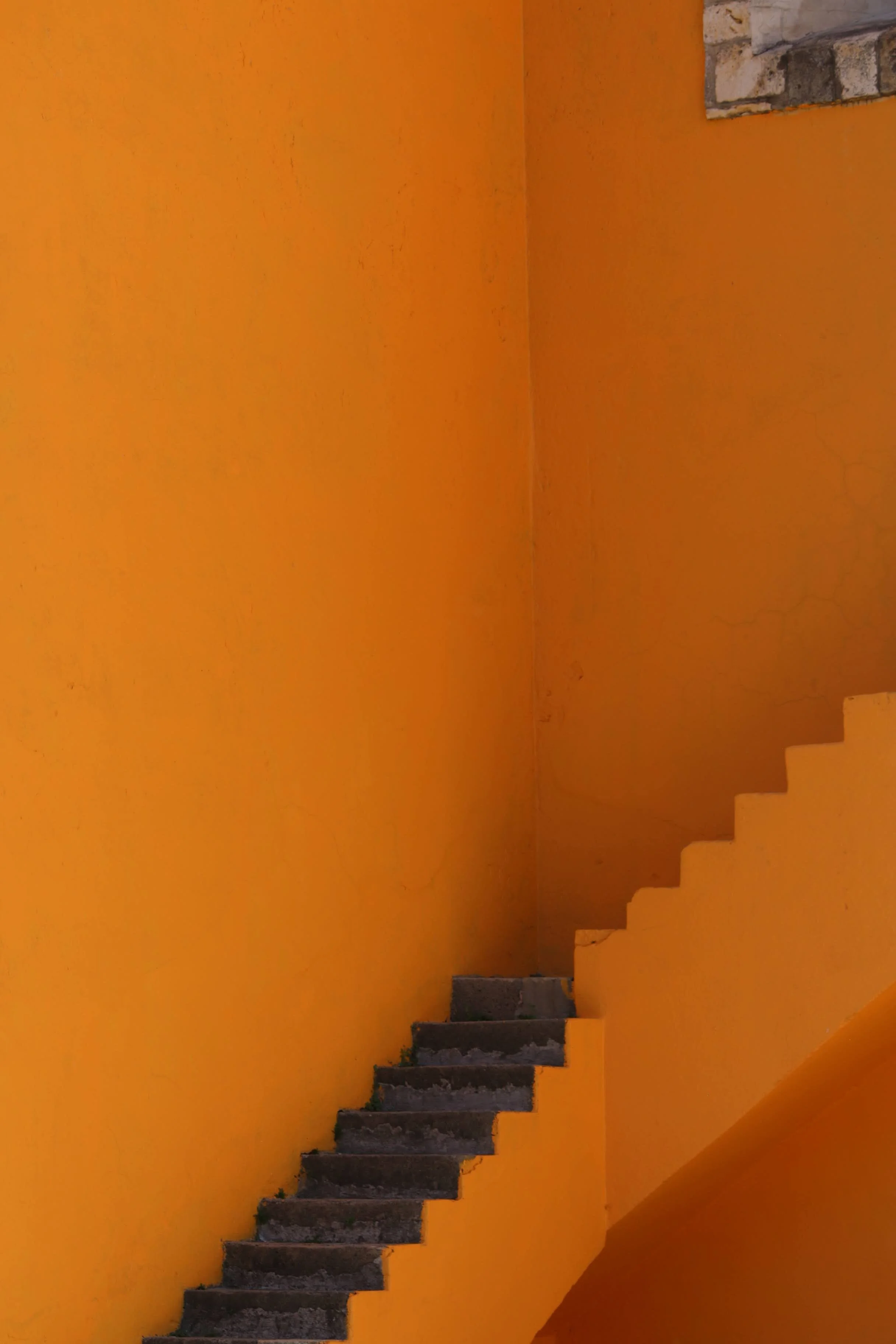 Orange staircase wall with visible steps leading up along a corner, with a small section of rocky wall at the top.