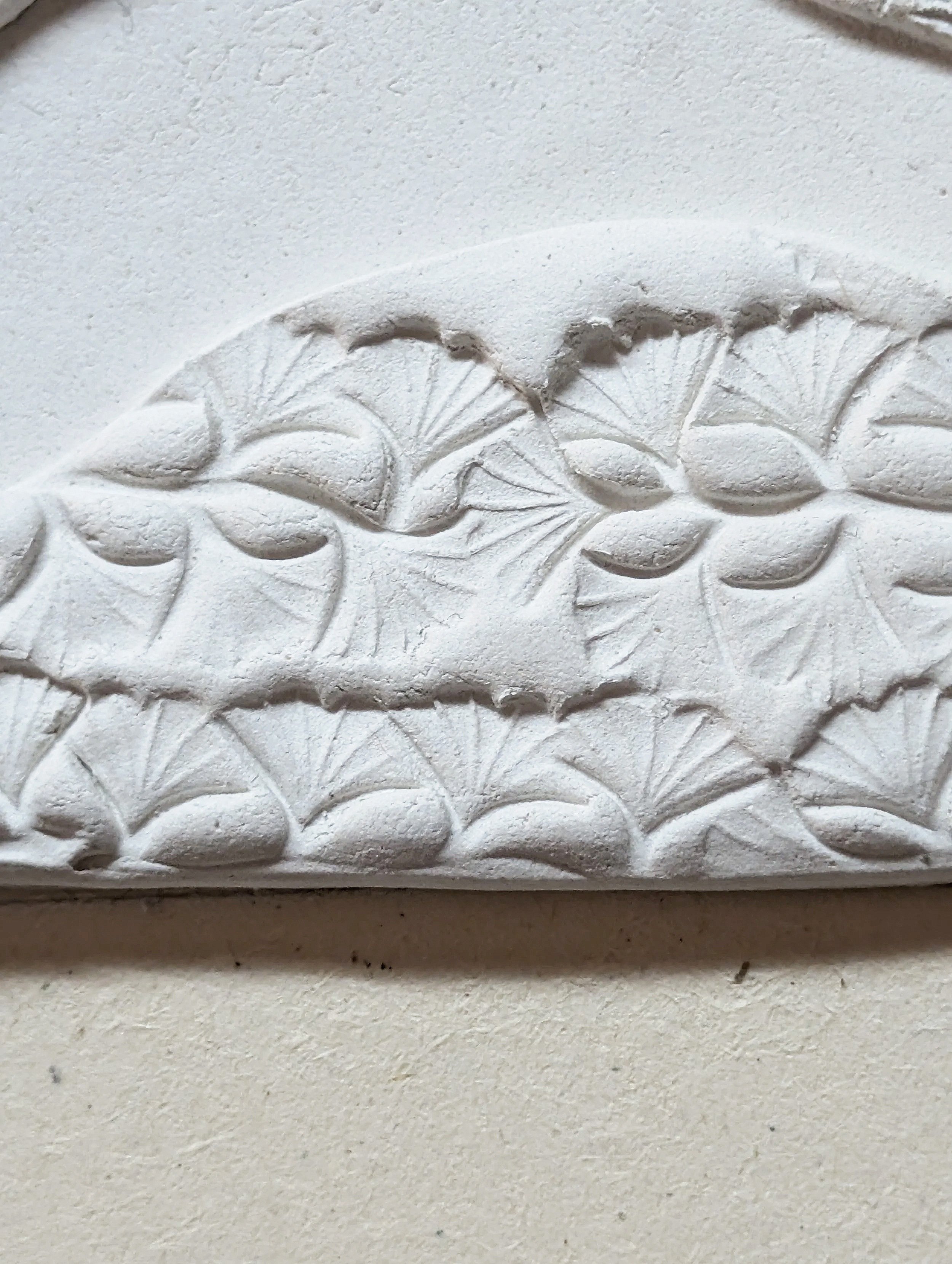 Close-up of a white decorative relief featuring intricate patterns of leaves and foliage on a wall.