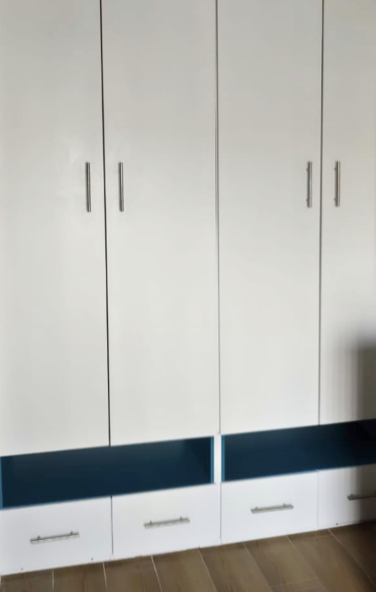 A white wardrobe with silver handles, mounted on a wall with wooden flooring.