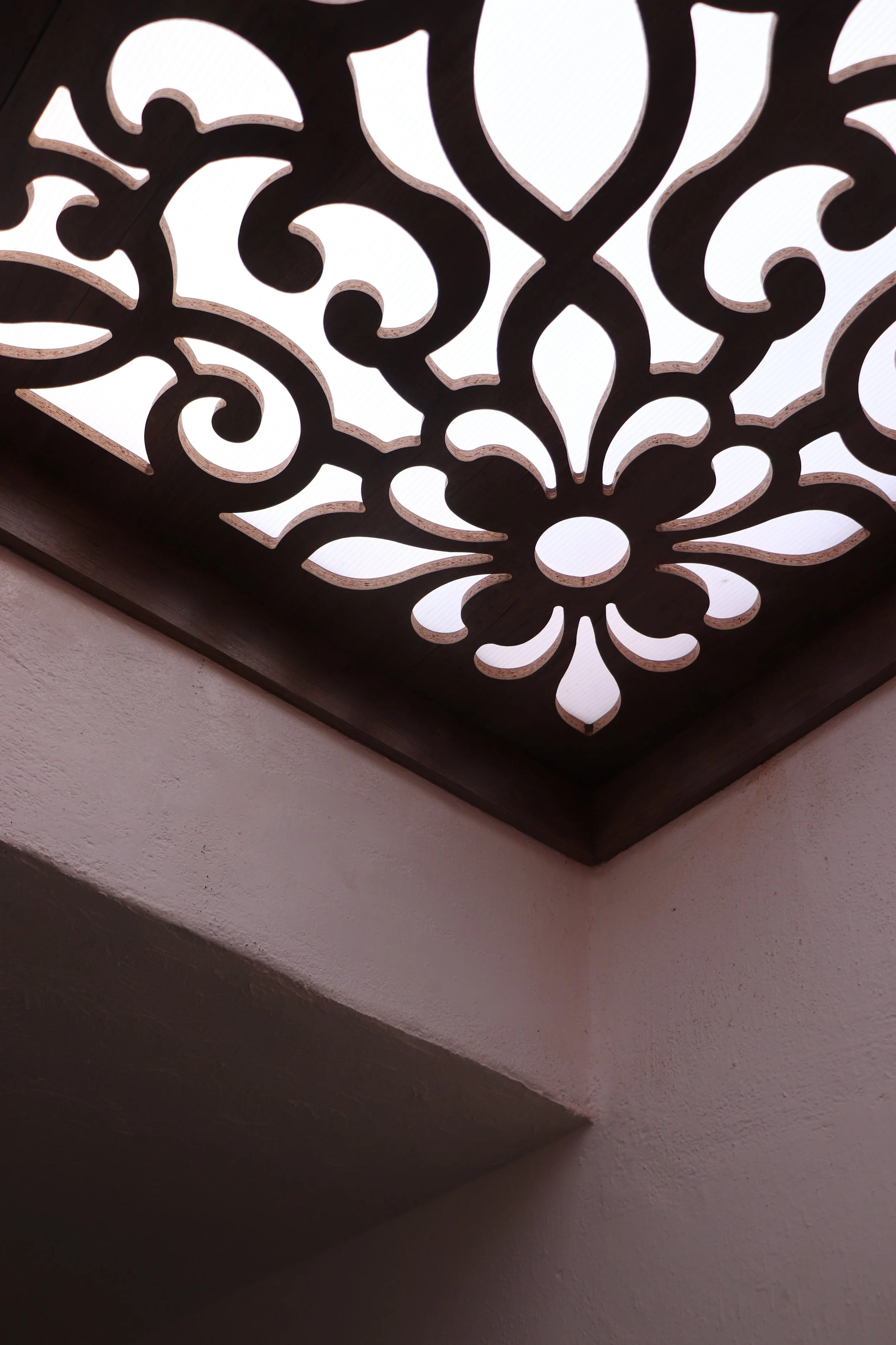 Decorative ceiling light with intricate floral and swirl cutout patterns, emitting bright white light.