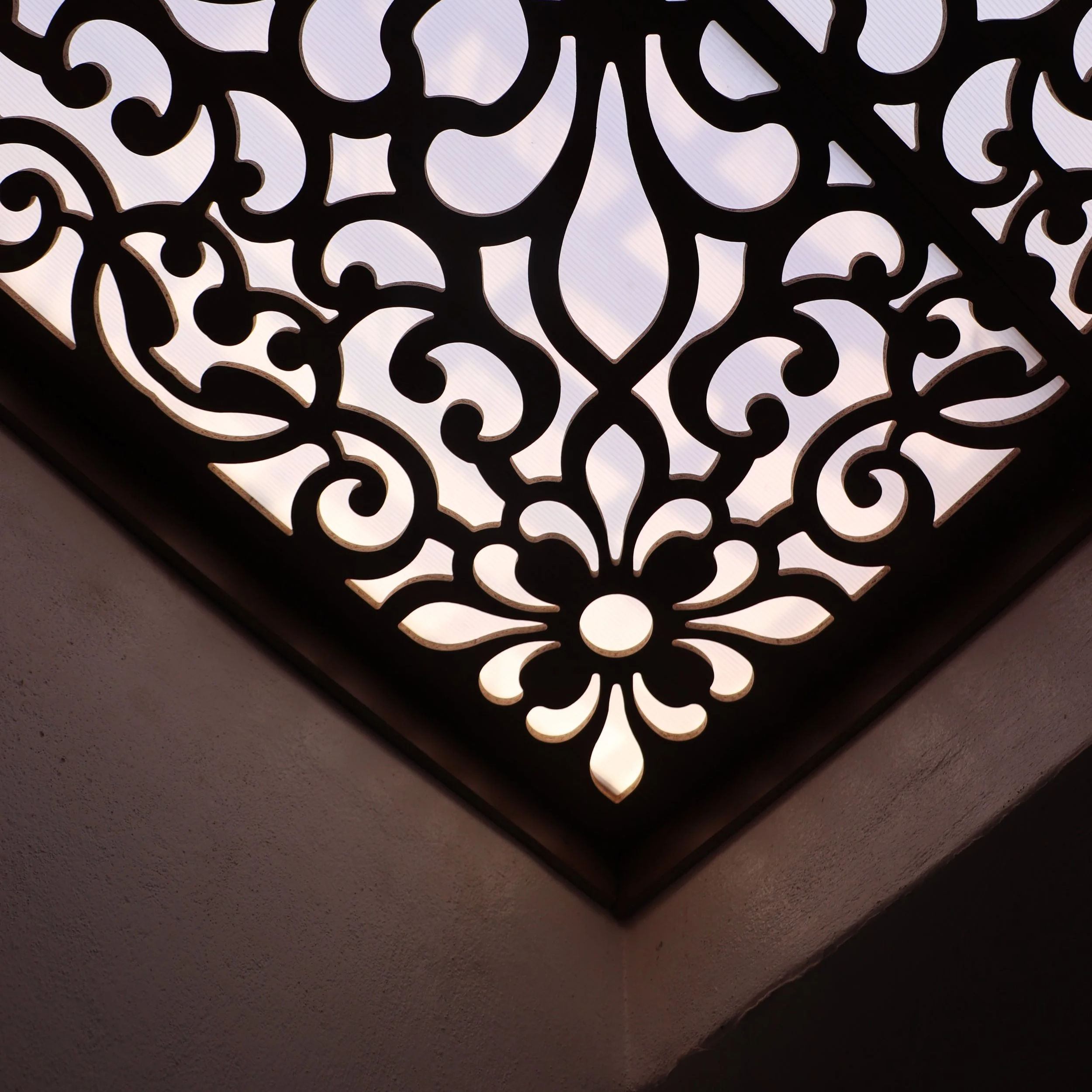 Close-up of an ornate light fixture with intricate cut-out patterns, mounted on a wall, illuminated from behind.