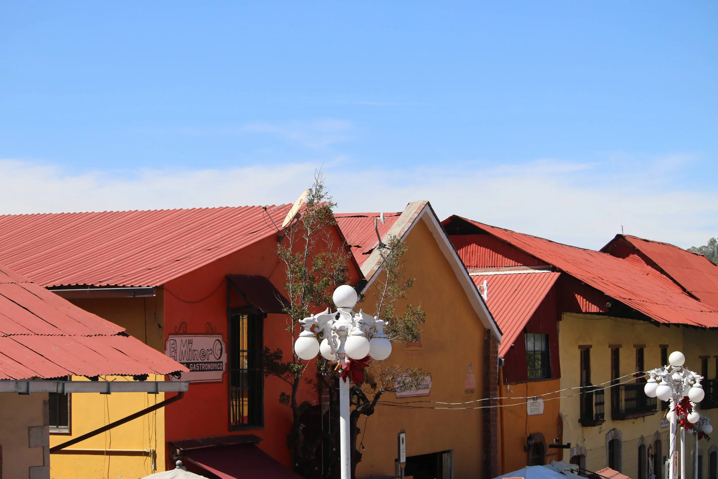Colorful buildings with red roofs and a bright blue sky, with decorative street lamps and trees in front.