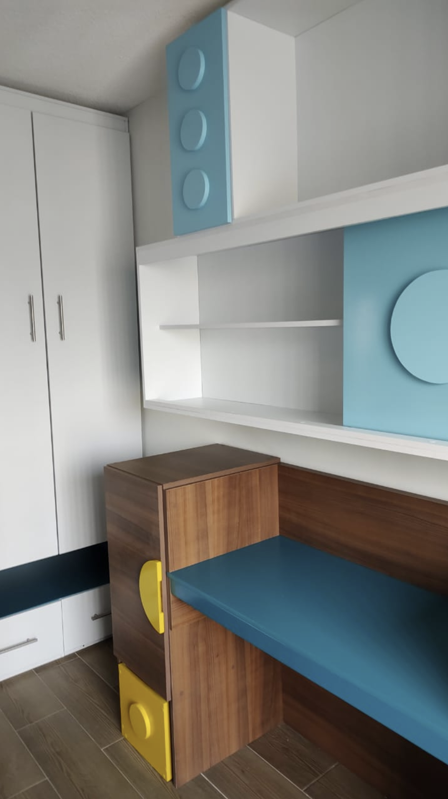 A corner of a room with white cabinets, blue and wood furniture, and a wooden floor.