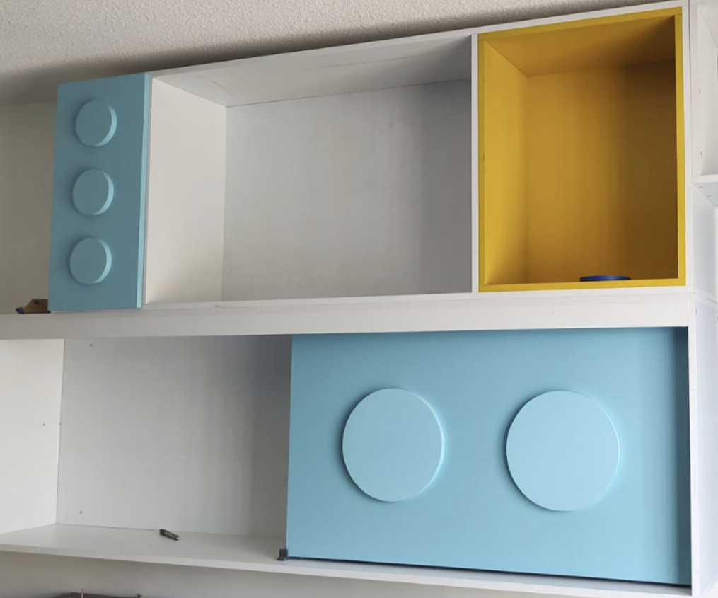 Colorful wooden toy storage unit with blue and yellow compartments and circular design elements.