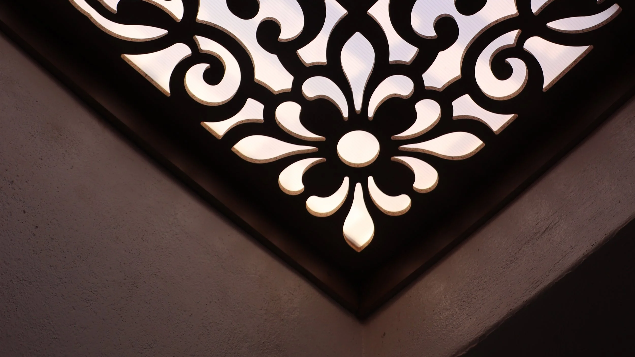 Decorative ceiling light fixture with ornate black design and soft white lighting, mounted at an angle on a textured ceiling.