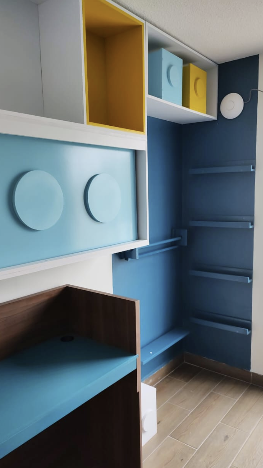 Colorful built-in shelves and drawers in a modern room with blue walls and wooden floors.