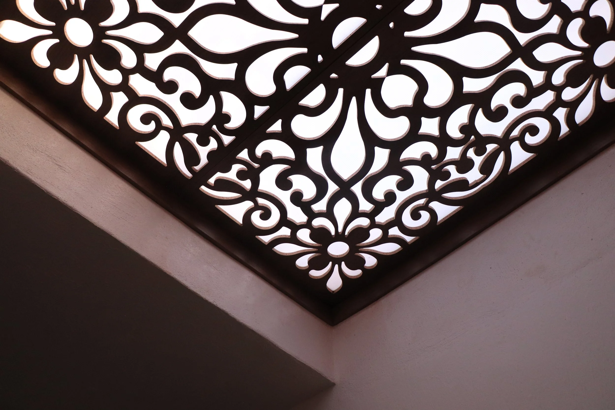 Decorative plafond with intricate gold-colored floral and swirl patterns, backlit with white light.