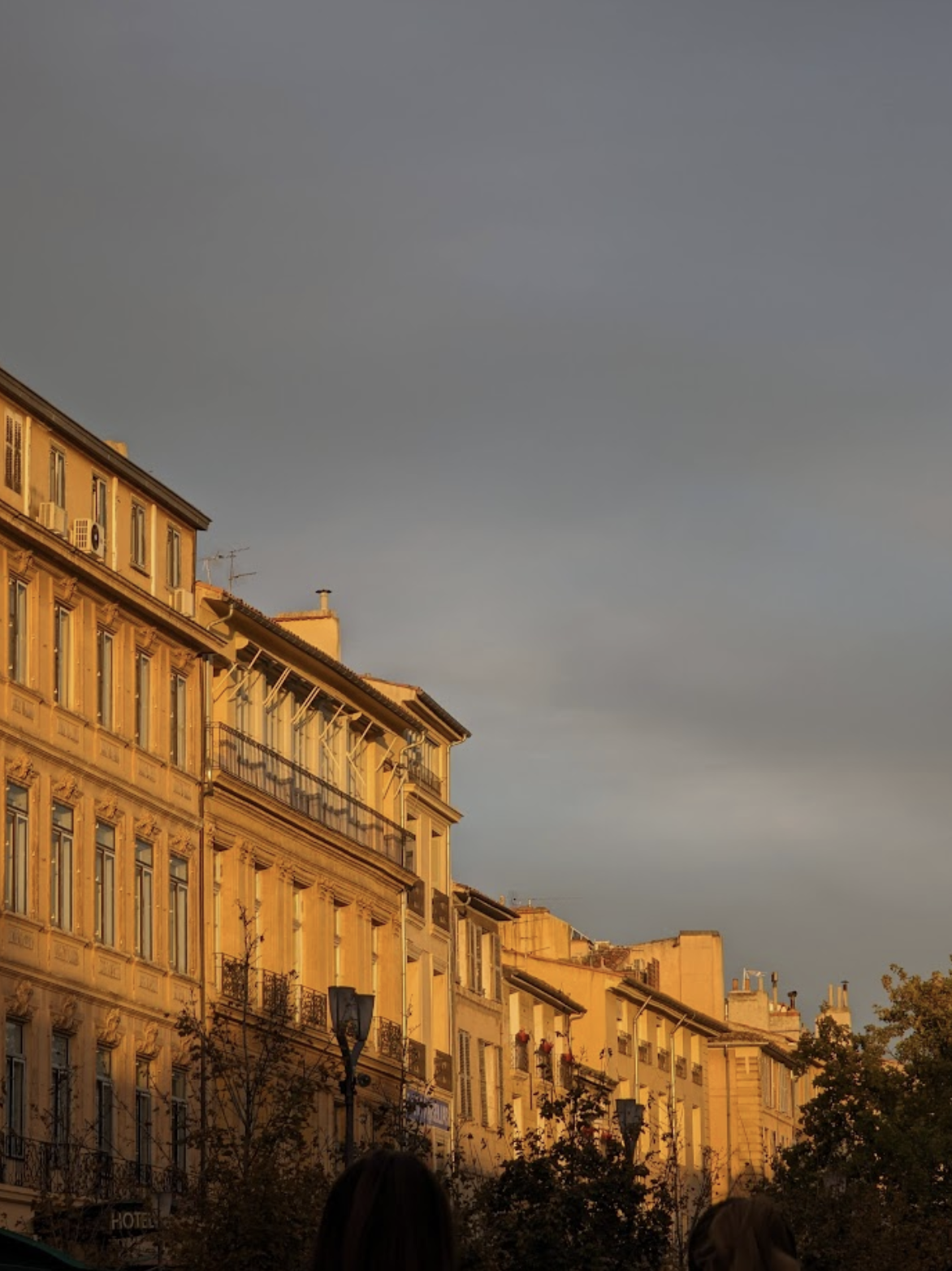 Image of Parisian apartment buildings illuminated by warm sunlight, with a dark cloudy sky in the background.