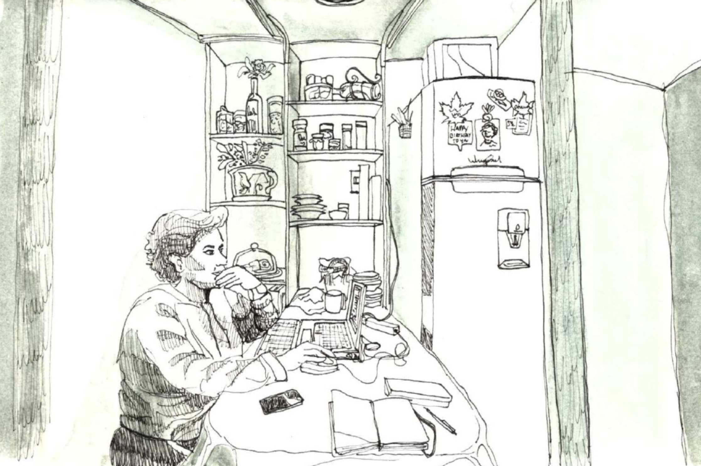 A person with glasses and short hair is sitting at a desk, with a computer, papers, and coffee cup. Behind them are shelves with jars, books, and decorations, and a small fridge with magnets on it.