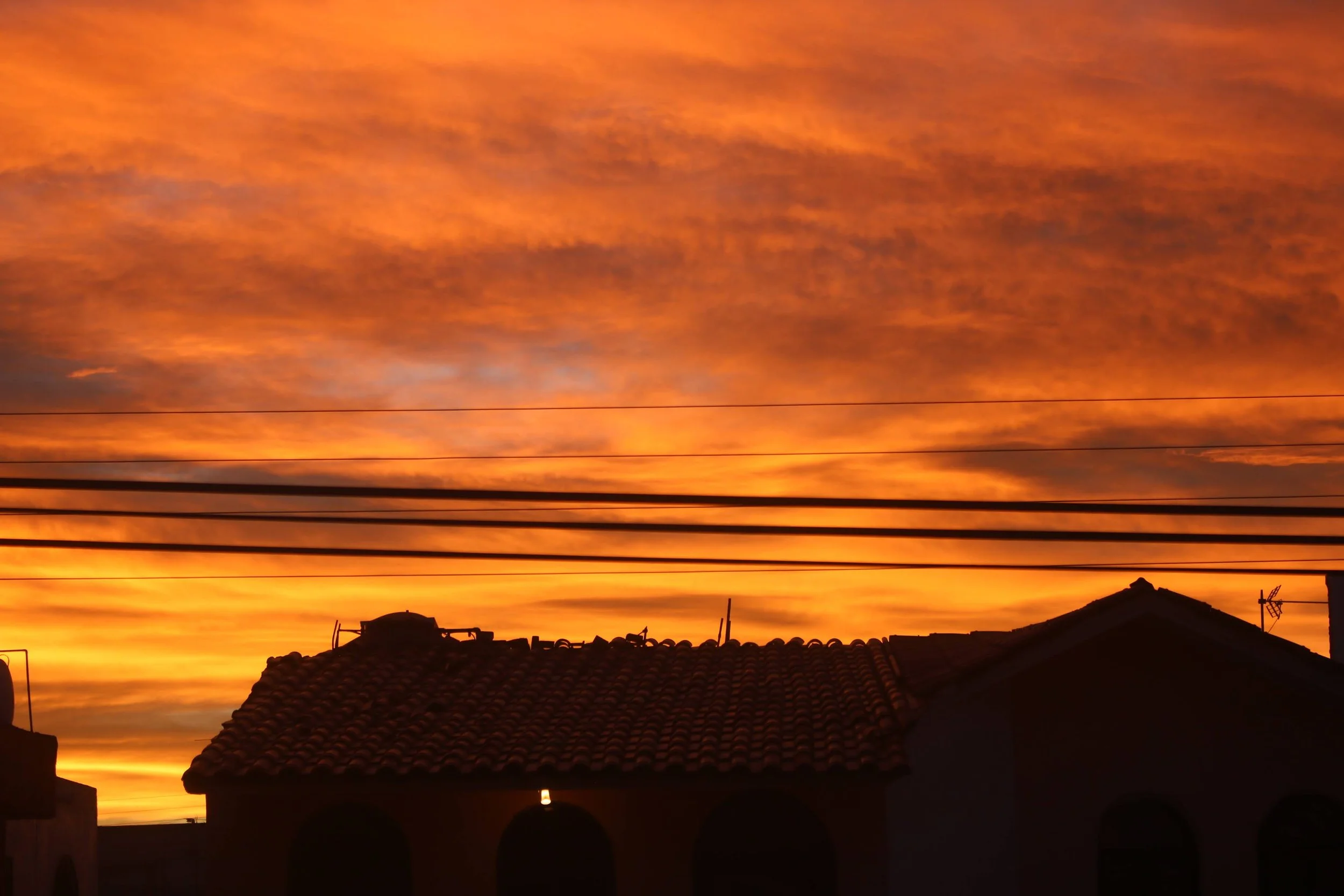 Sunset sky with orange clouds over rooftops and power lines in a residential area.