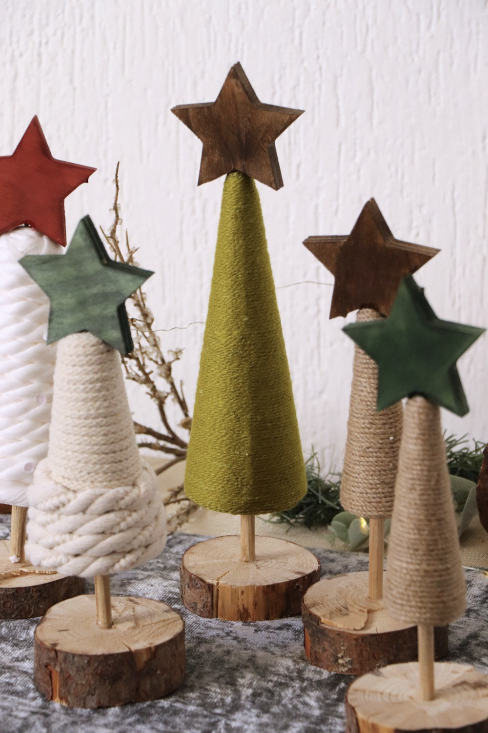 Decorative Christmas trees made of yarn and wood with star toppers on a textured surface.