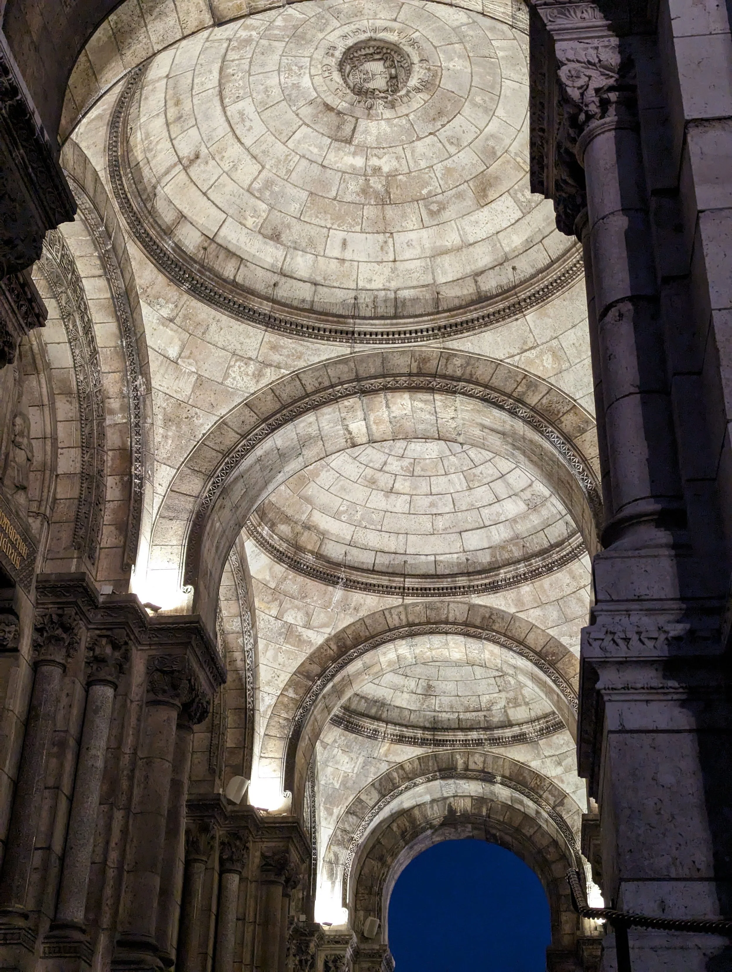 View of a classical archway with ornate stone columns and decorative moldings, taken from below during daytime.