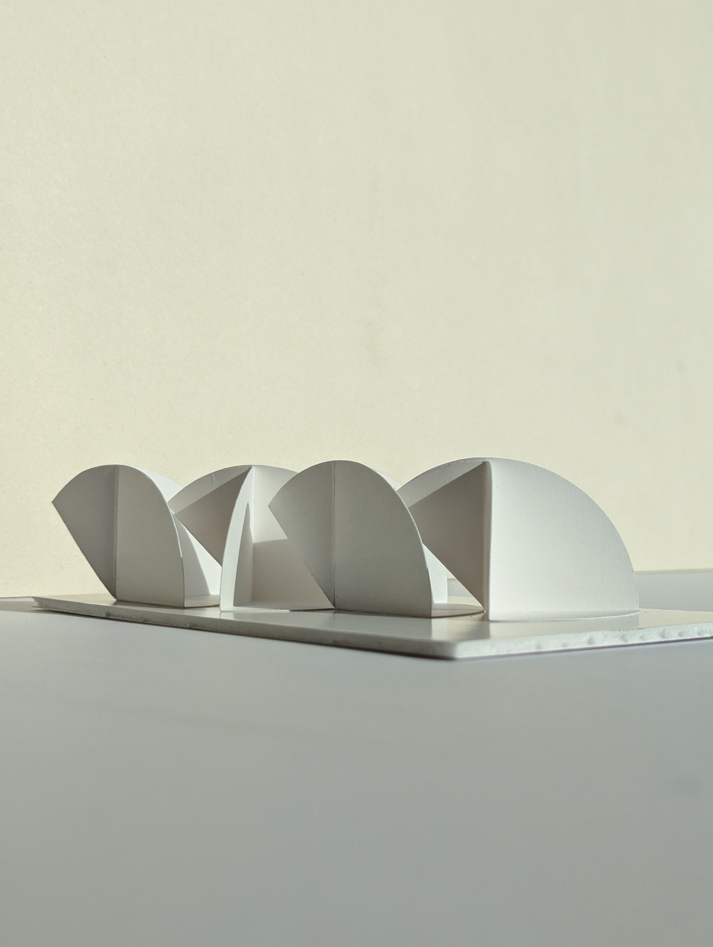 Close-up of a white architectural model with curved, semi-spherical elements on a flat base, against a plain, light-colored background.