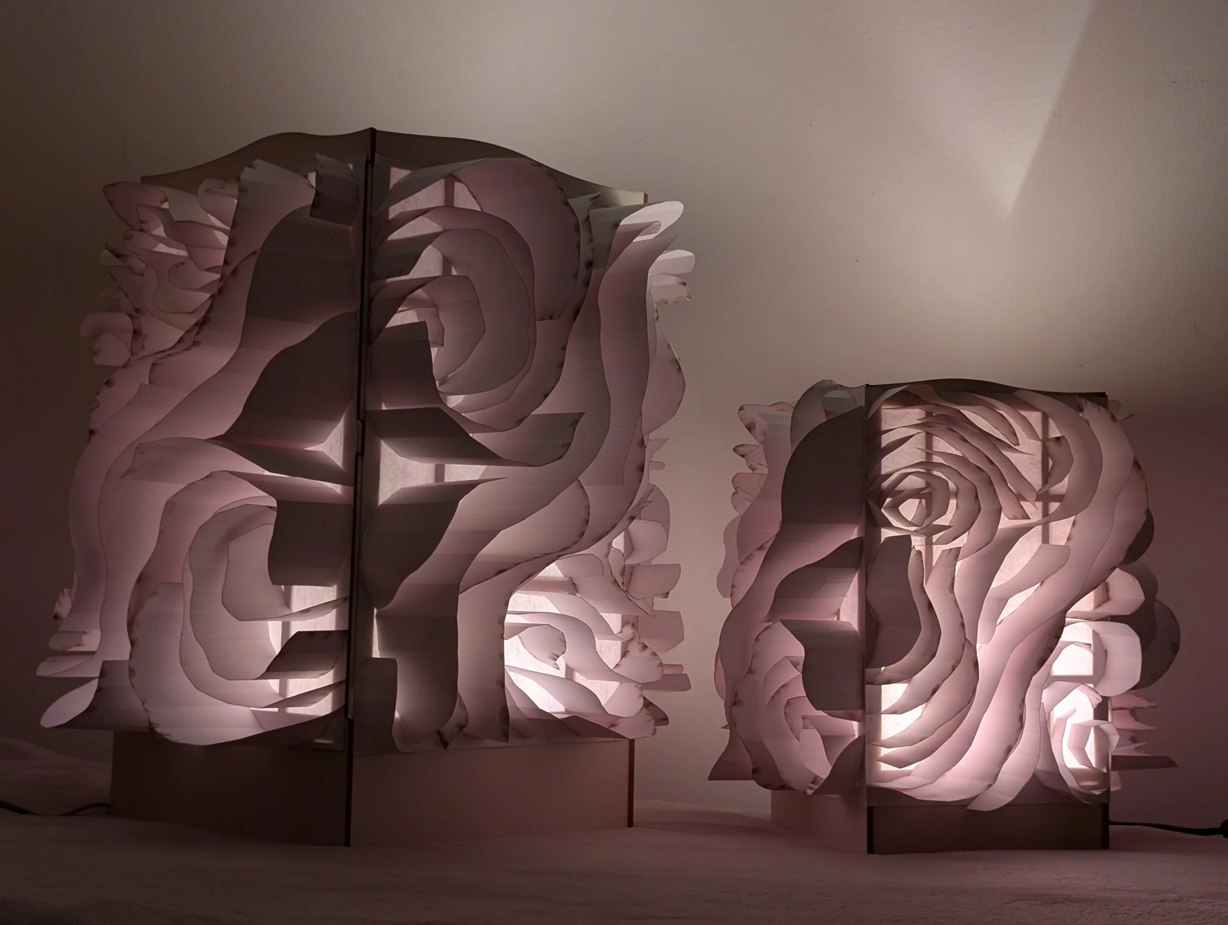 A large, abstract, three-dimensional wall sculpture made of layered, petal-like shapes illuminated with soft pink lighting.