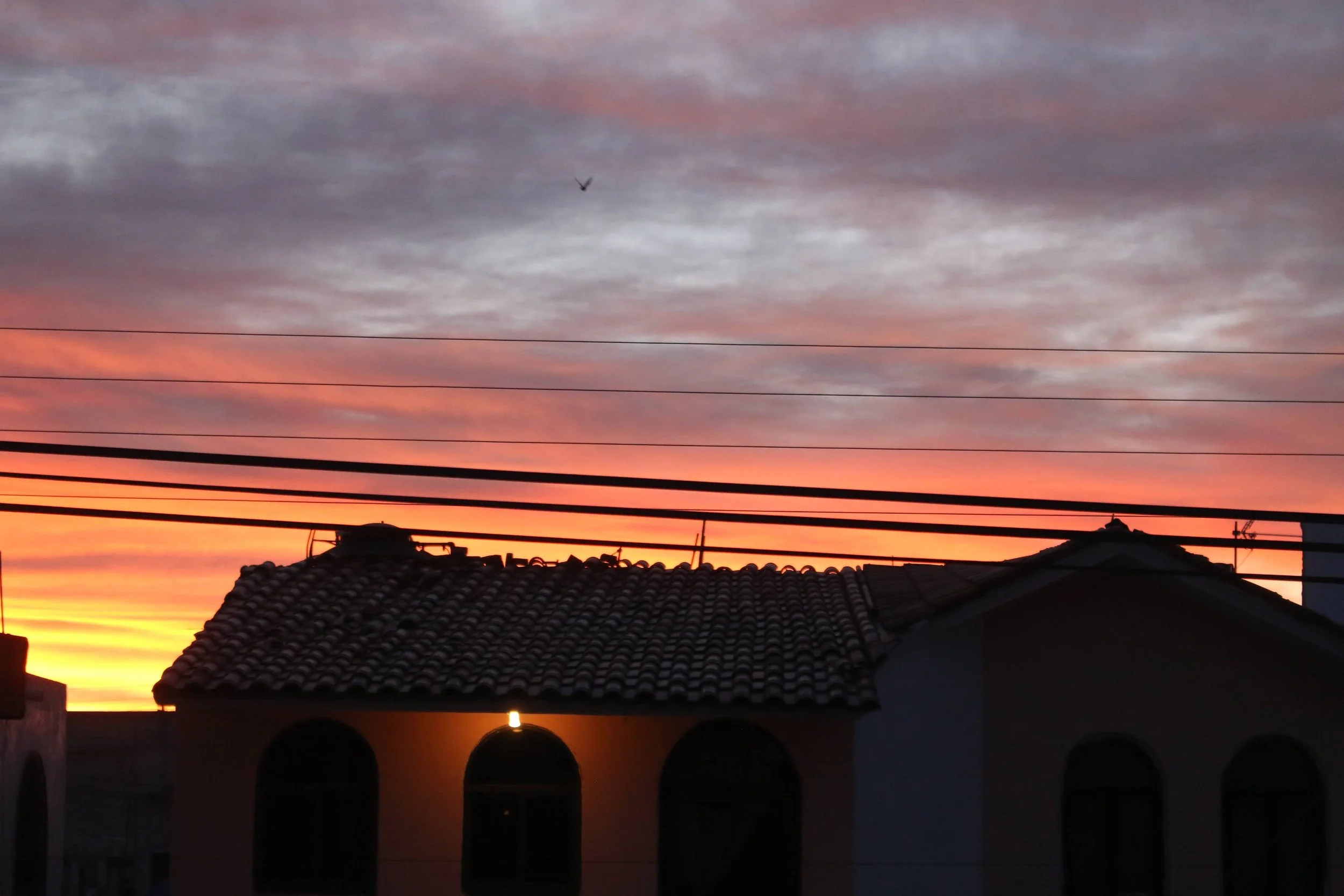 Sunset sky with pink, purple, and orange clouds above silhouetted buildings with tiled roofs and power lines.