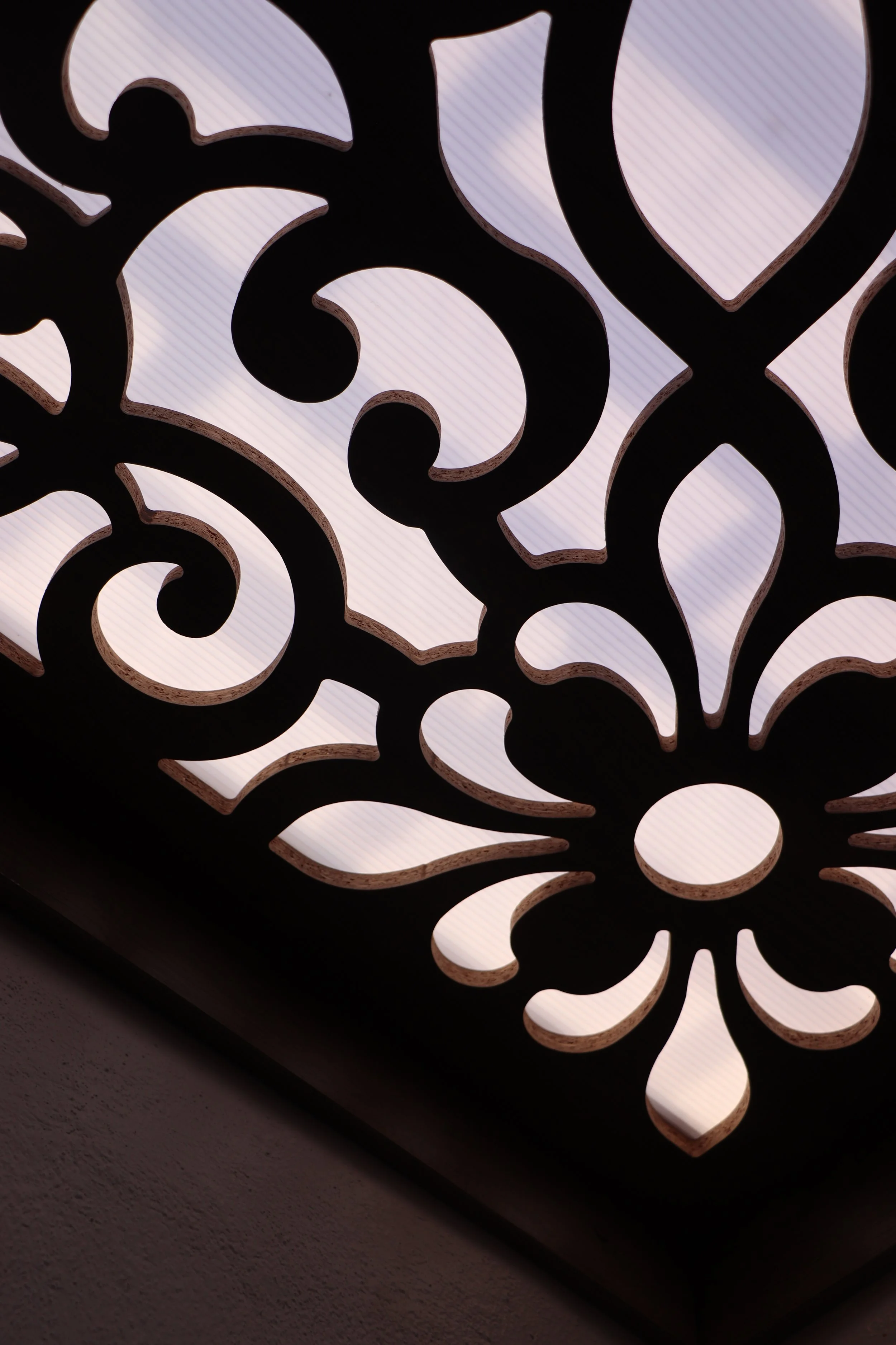 Close-up view of an ornamental light fixture with intricate, swirling cutouts, backlit to highlight the pattern.