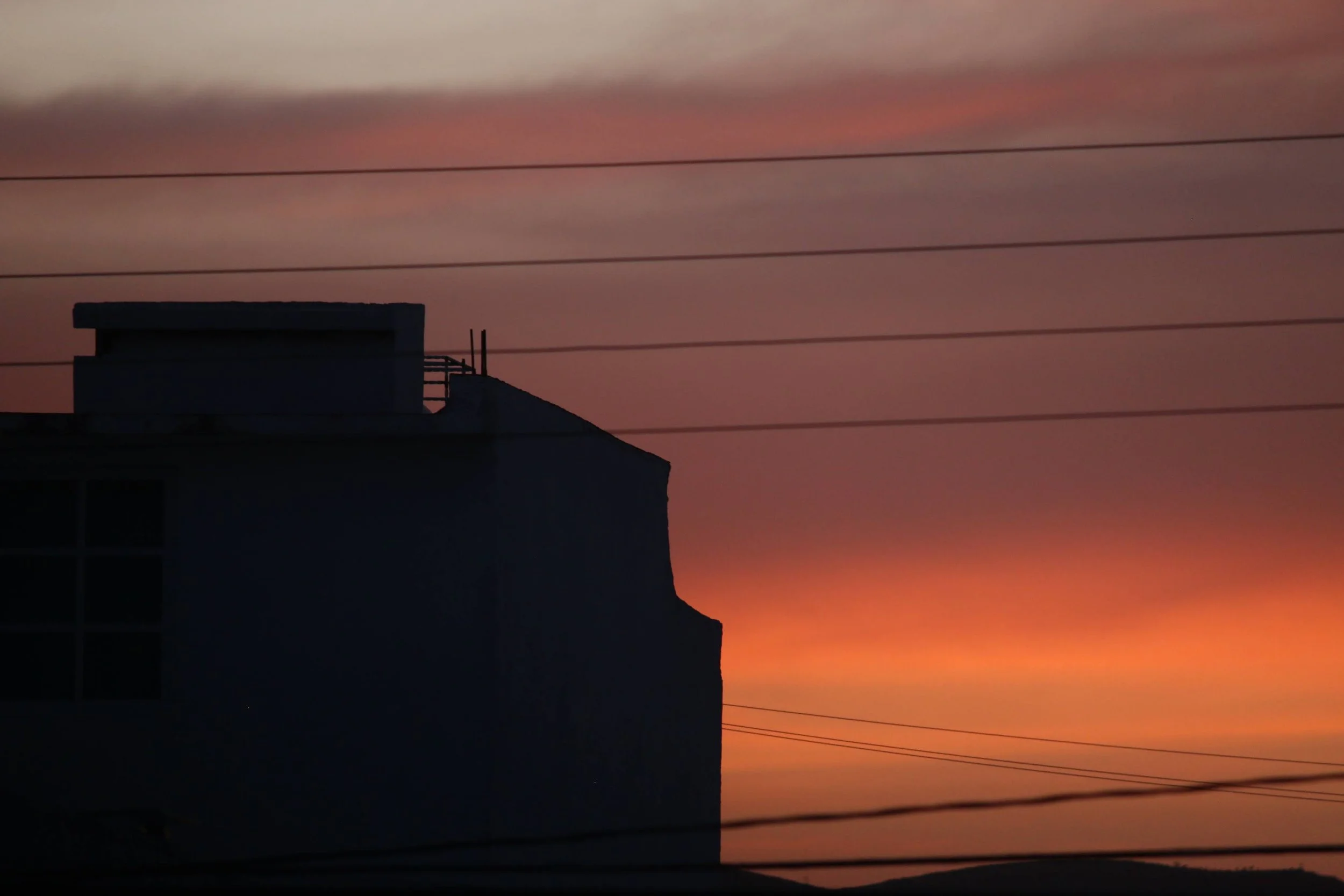 Silhouette of a building against a colorful sunset sky with horizontal power lines.