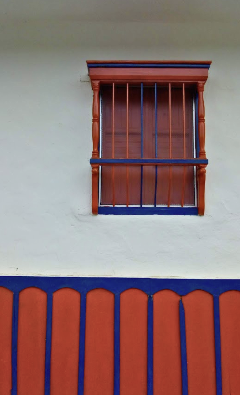Close-up of a decorative wall with a small window featuring wooden and metal bars, and a colorful border at the bottom.