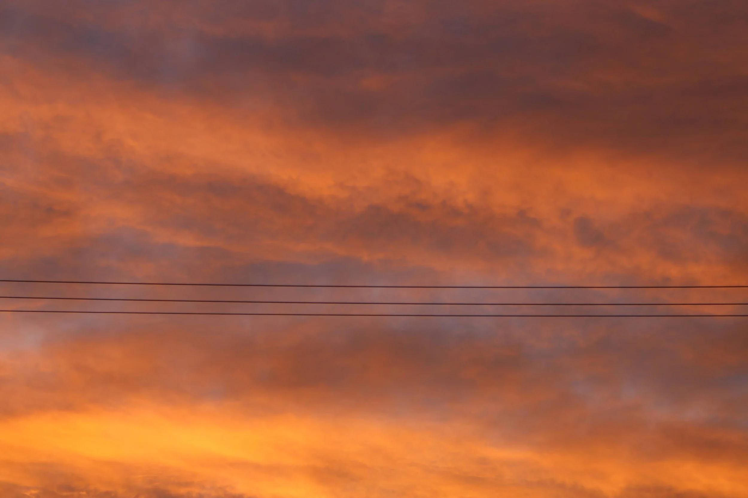 A sky filled with orange and purple clouds during sunset, with horizontal power lines at the bottom.