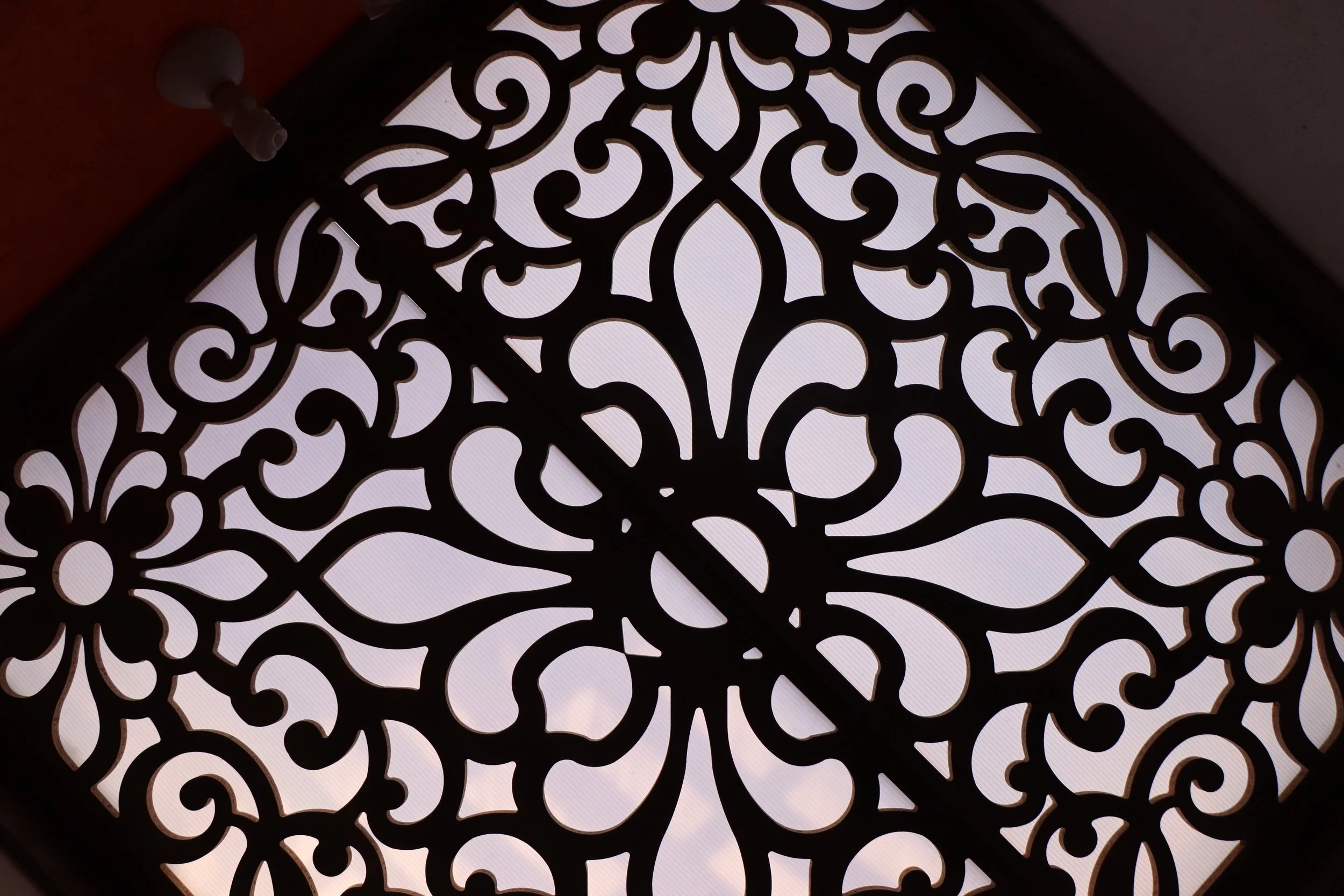Close-up of an ornate, black, decorative metal or wood panel with intricate swirling patterns, illuminated from behind.