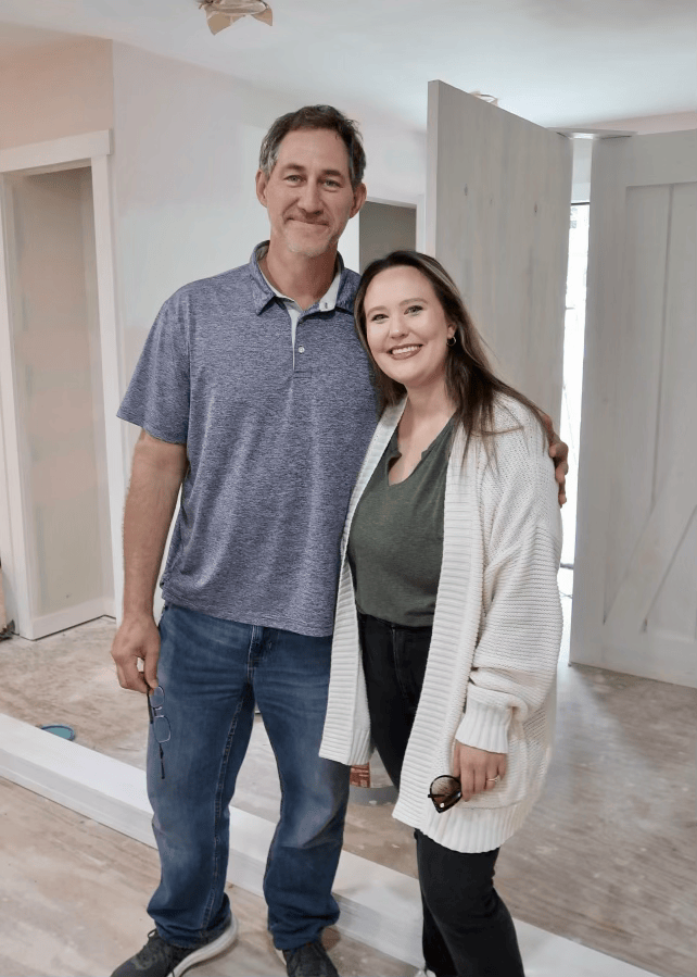 A man and woman smiling and standing close together , in front of a partially open sliding door.