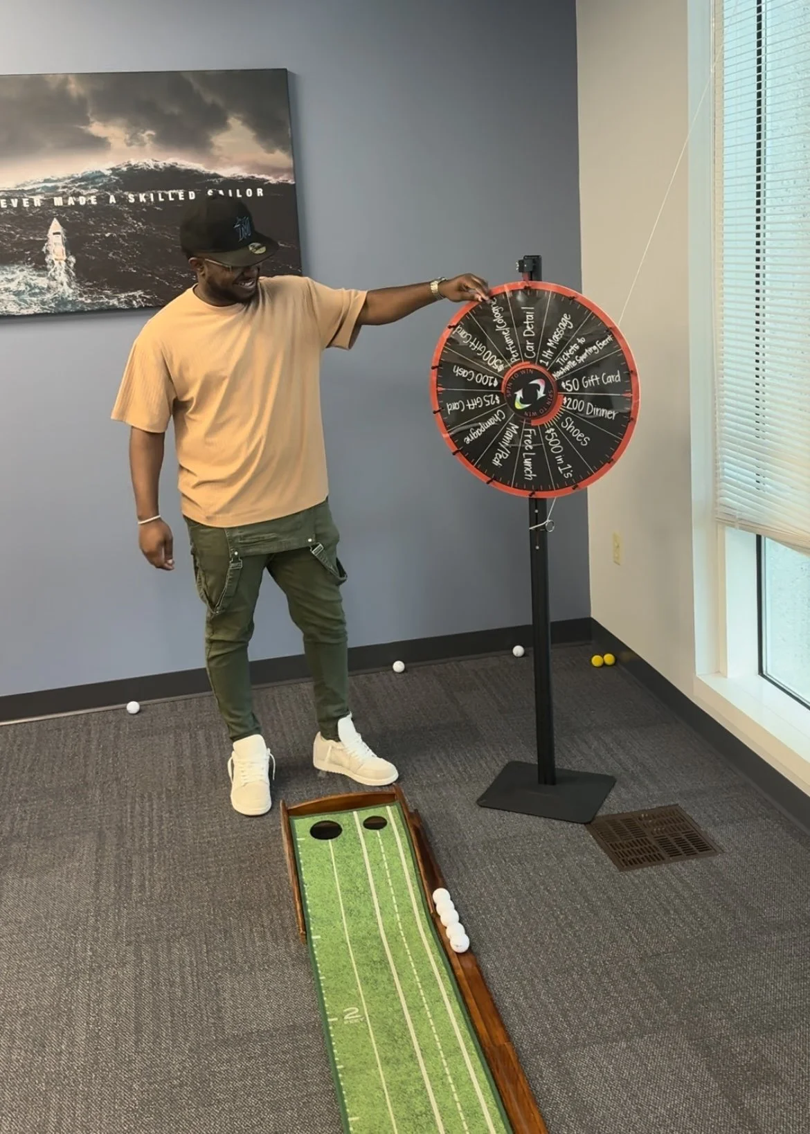 Man playing a game of carnival-style golf, hitting golf balls towards a target on a mini-golf lane, with a spinning wheel game in the background.