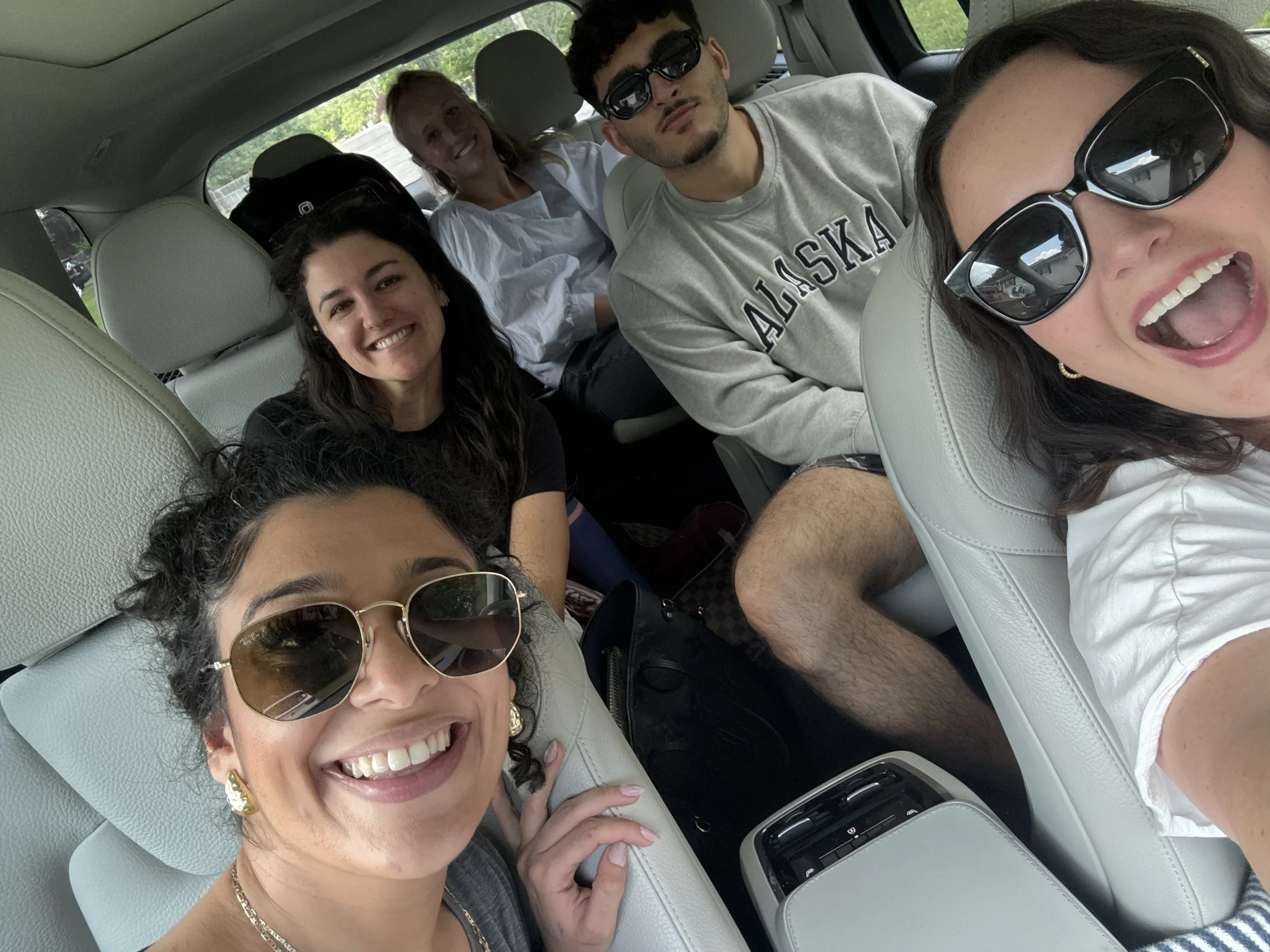 A group of five Canvas Homes teammates smiling and taking a selfie inside a car, with a woman in sunglasses in the foreground and four others in the back seat.