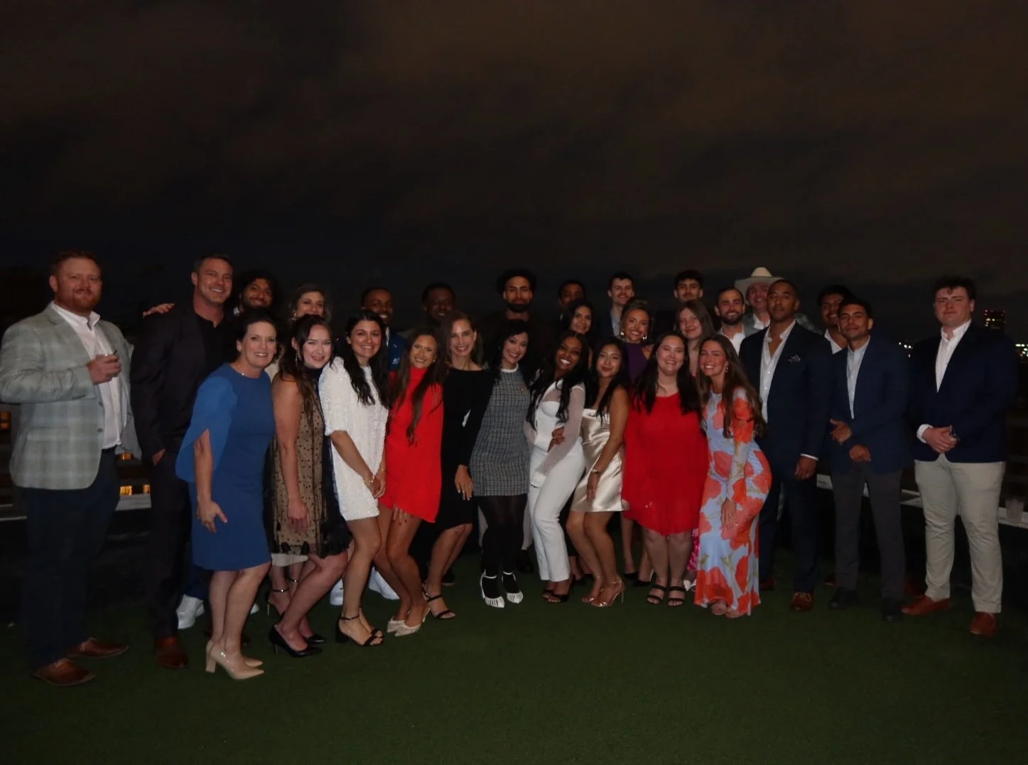 The Canvas Homes team dressed in formal and semi-formal attire posing on a rooftop at night. The group includes men and women smiling for the camera, with a dark sky and city lights in the background.