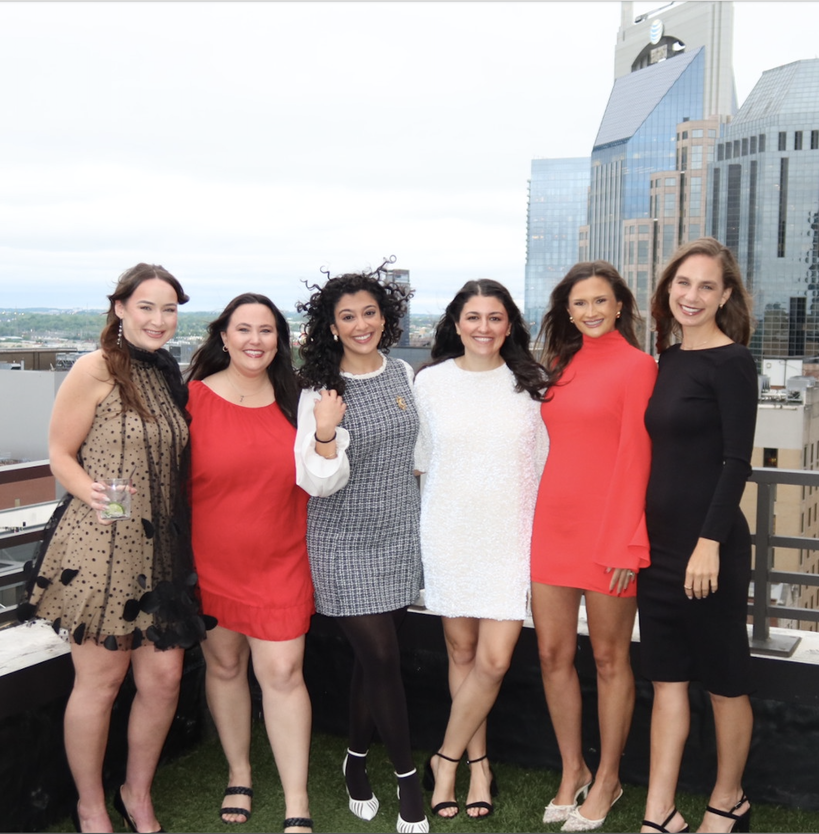 A group of six women from the Canvas Homes team standing together on a rooftop with city skyscrapers in the background, smiling and dressed in stylish attire.