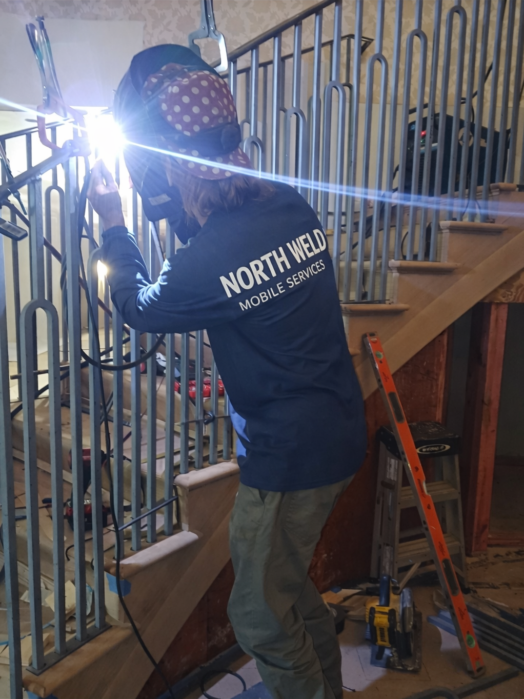 A worker from North Weld Mobile Services installing or repairing metal railings on a staircase inside a building.