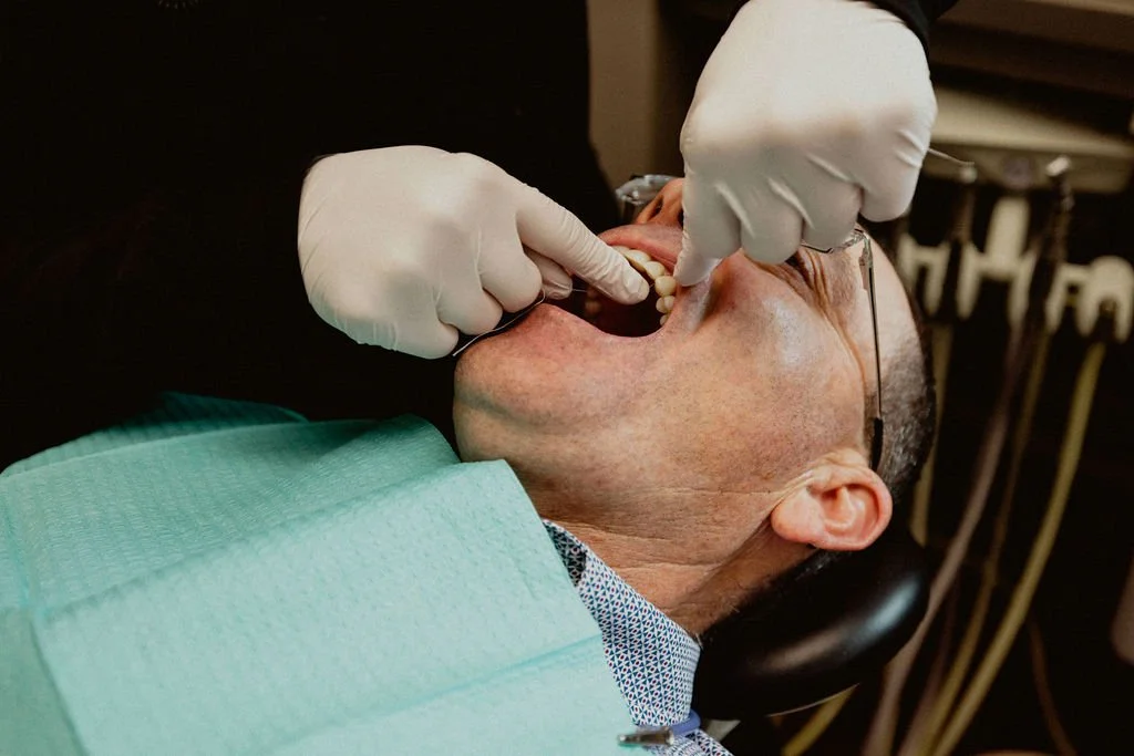 A dentist wearing gloves examines a patient's open mouth during a dental checkup.