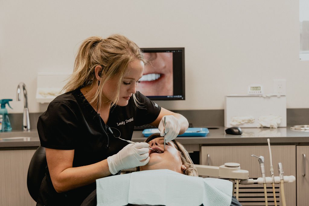 Dentist performing a dental procedure on a patient in a dental office with dental tools and a monitor in the background.