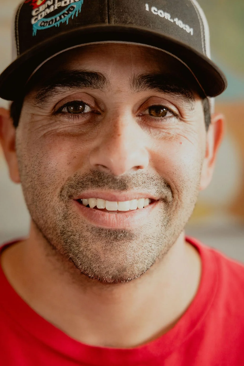 Close-up of smiling man wearing a black baseball cap and red shirt.