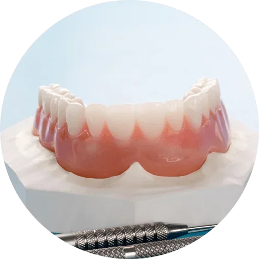 A dental prosthetic or denture with teeth set on a pink gum base, placed on a white surface with dental tools nearby.