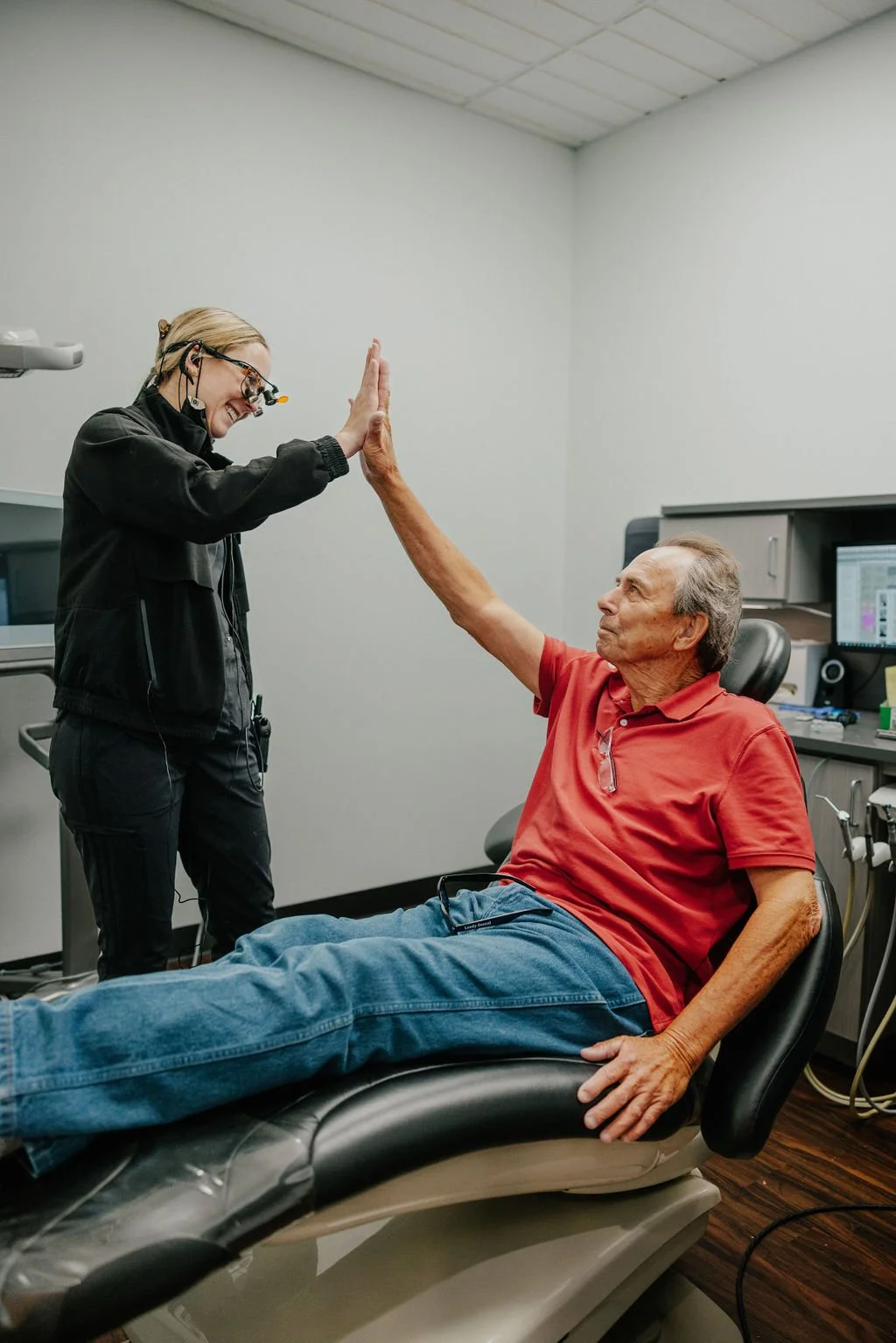 A healthcare professional giving a high five to an elderly male patient lying on a hospital bed in a medical office.