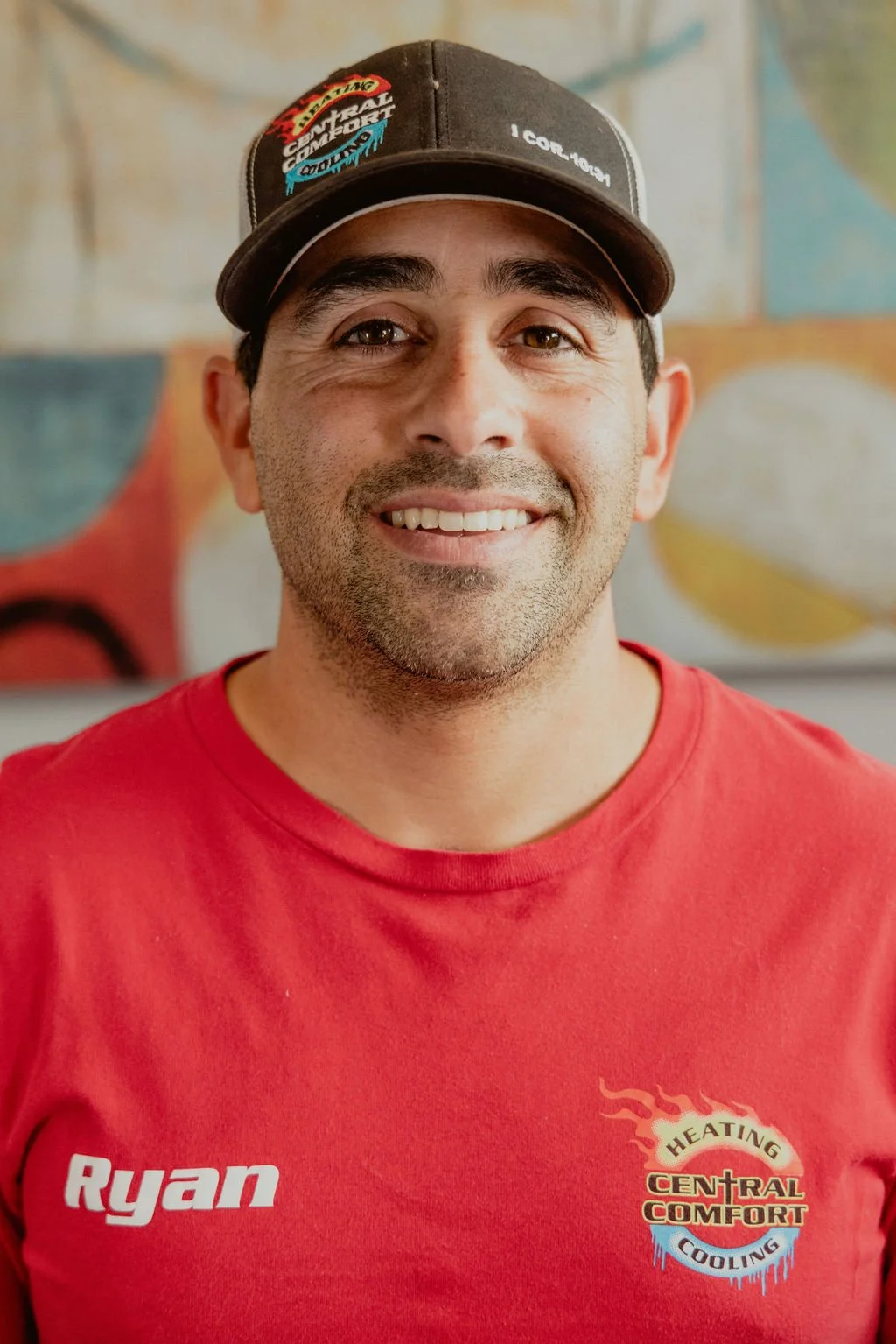 A smiling man wearing a black cap and a red shirt with the name Ryan and a heating and cooling service logo.
