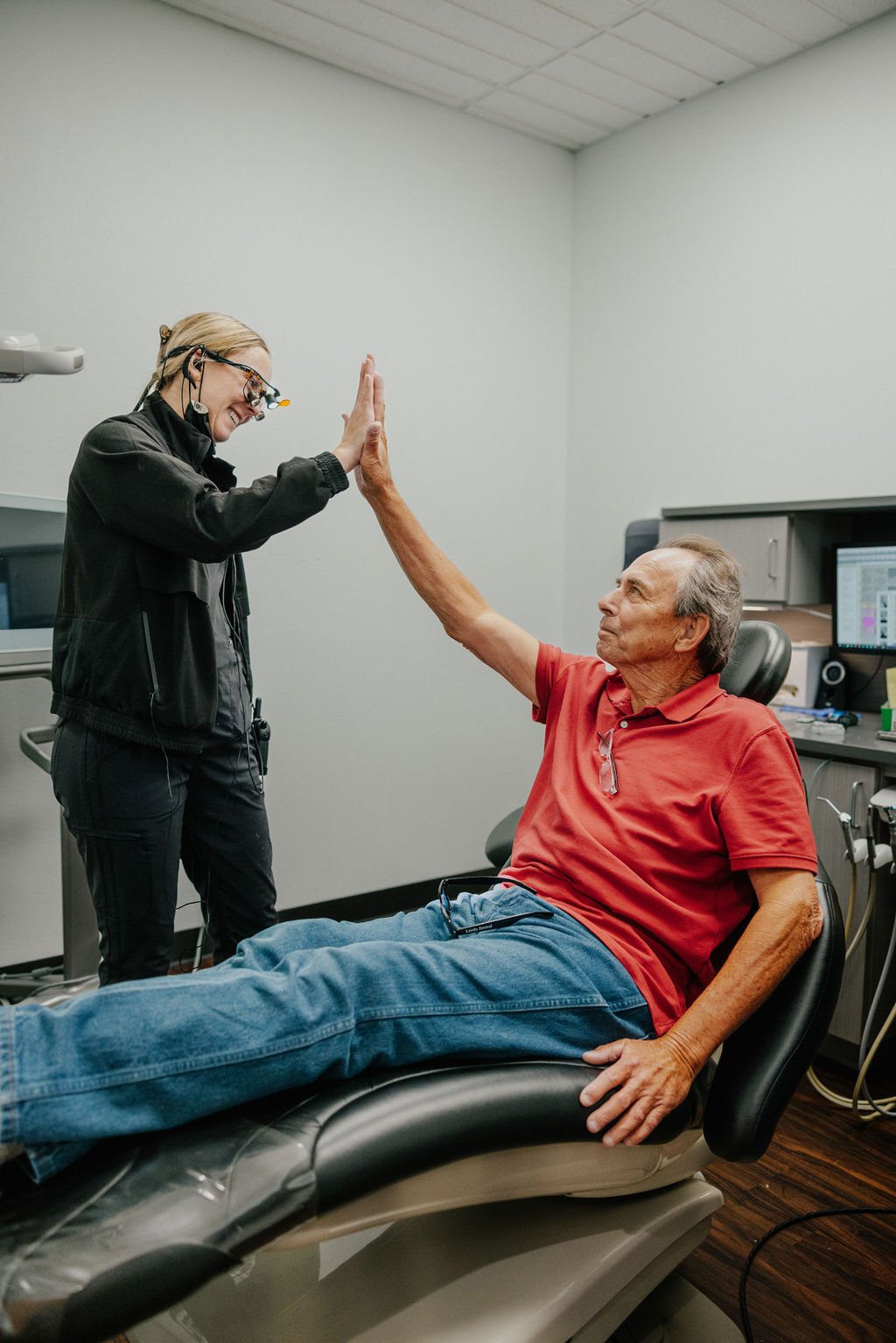 A female healthcare professional and an elderly man giving each other a high five in a medical examination room.