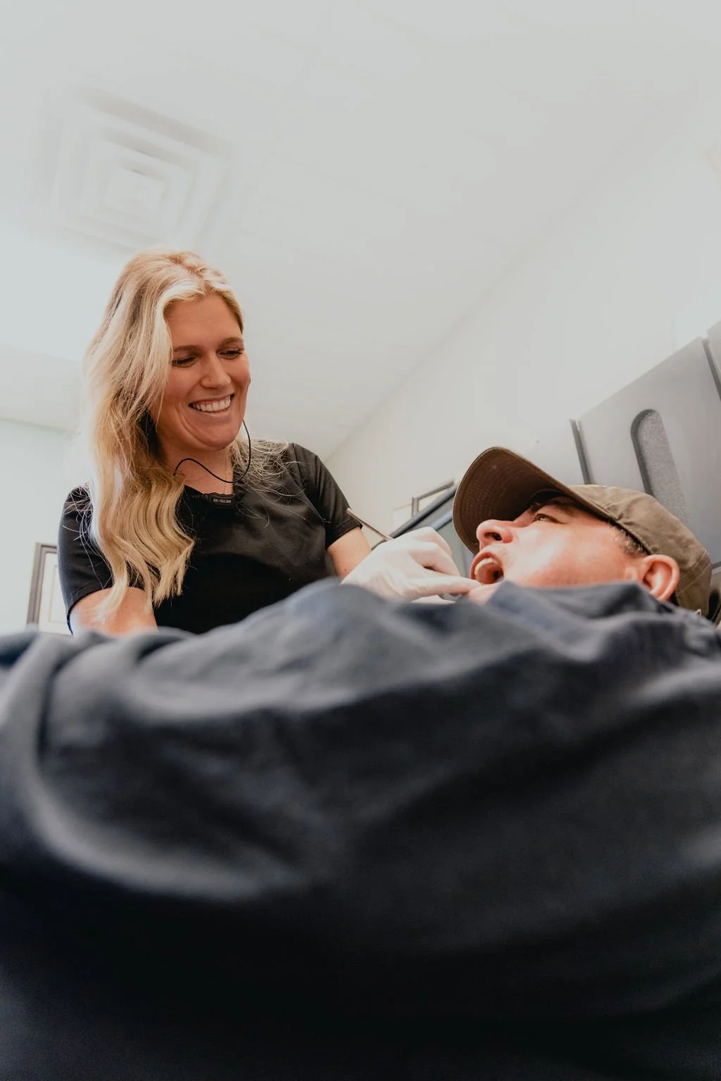 A female healthcare worker smiling at a patient lying on a medical bed, with the patient talking to her, in a clinical setting.