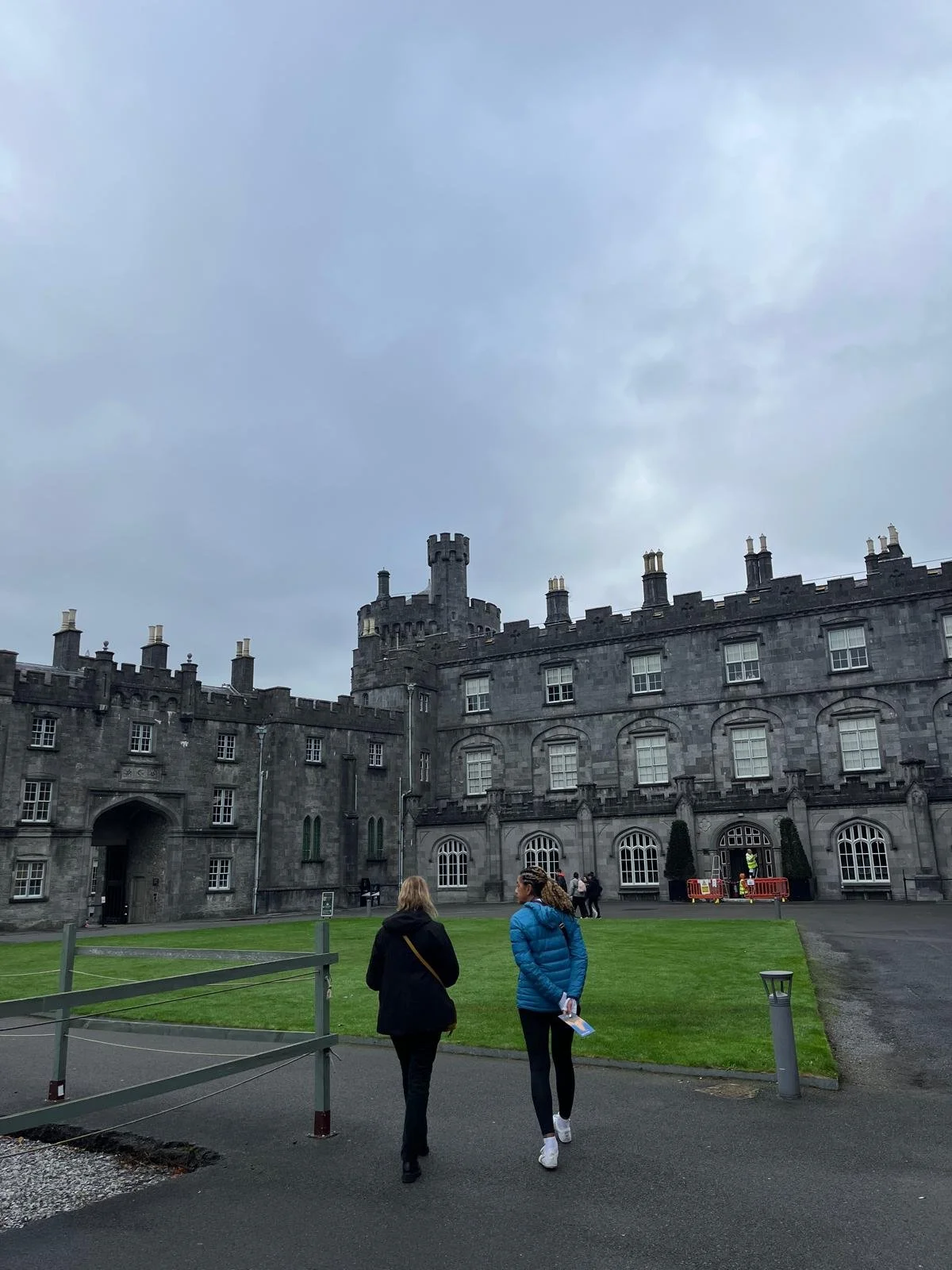 Scottish castle with stone walls and multiple chimneys, people walking on a path outside, cloudy sky