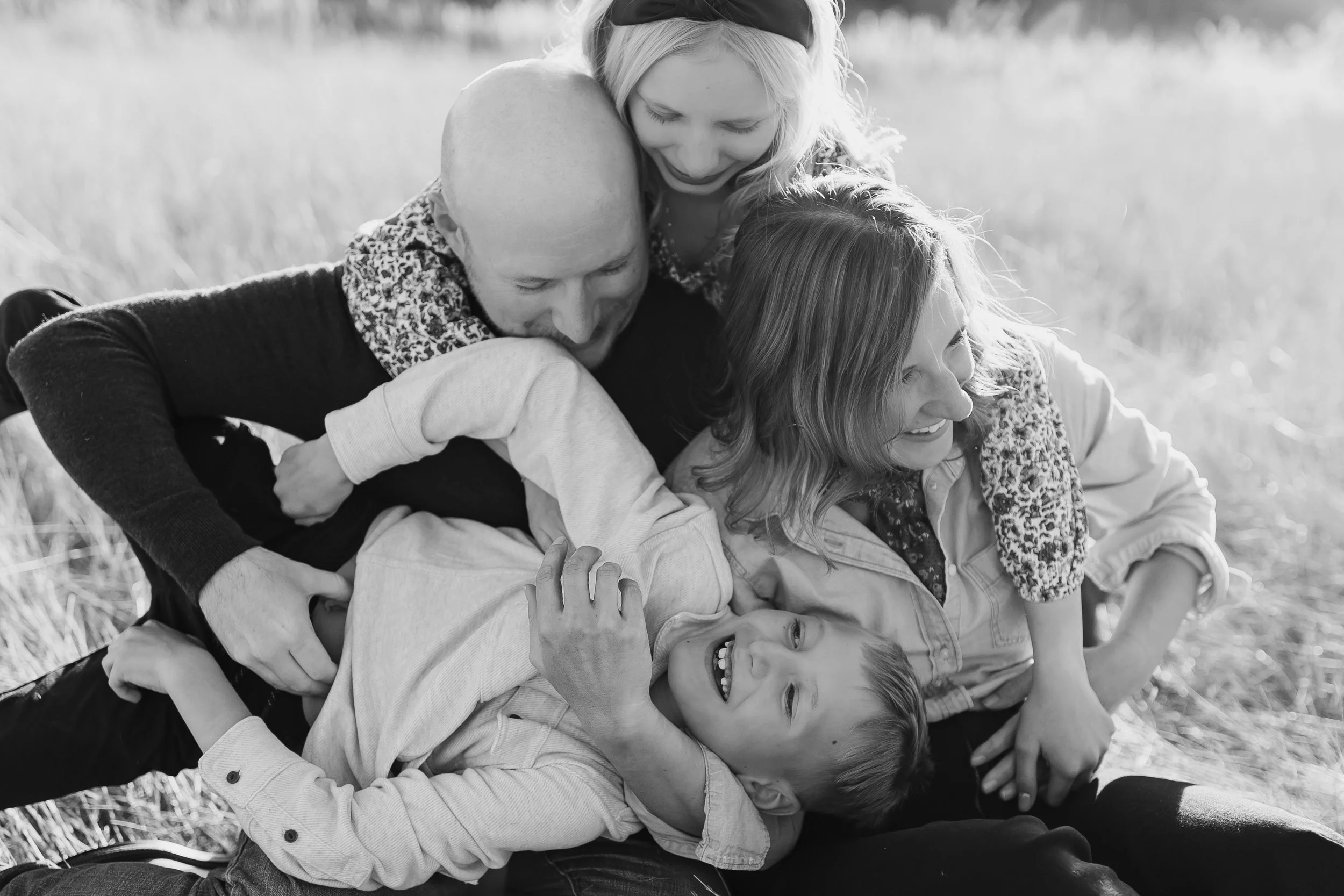 A black and white photo of a group of four children playing and wrestling on the grass, laughing and having fun.