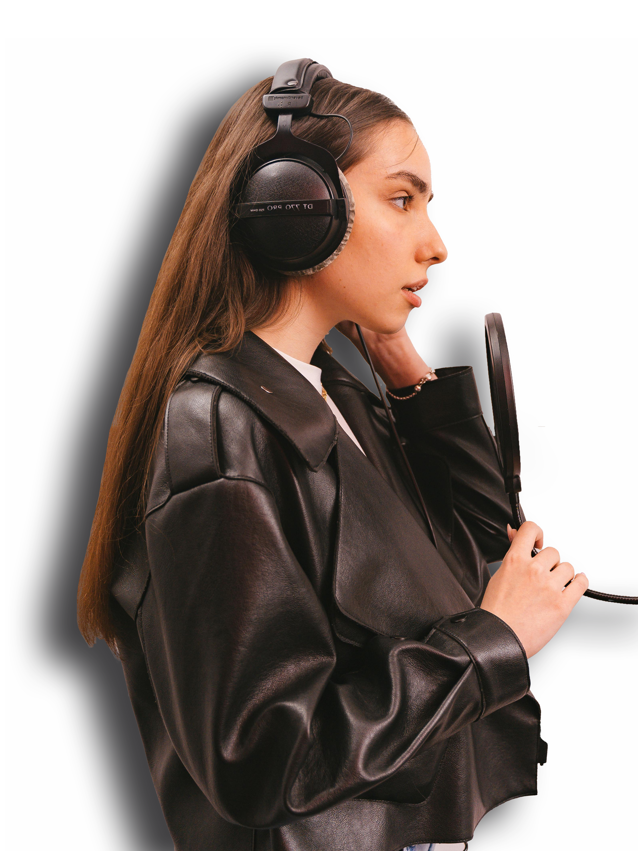 A woman wearing large over-ear headphones and a black leather jacket, speaking into a microphone against a dark background.