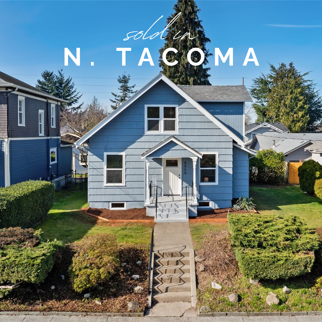 A blue house with a gabled roof, surrounded by well-maintained shrubs and a lawn, with a pathway leading to the front porch, in North Tacoma.
