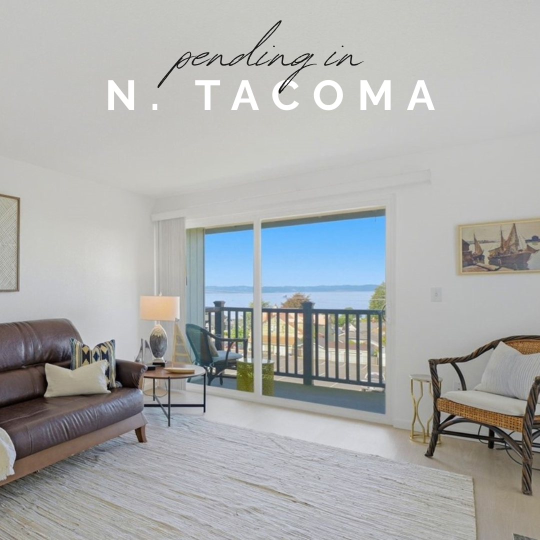 Living room with a sliding glass door leading to a balcony with a view of water and sky, furnished with a brown leather sofa, armchair, side table, and decor.
