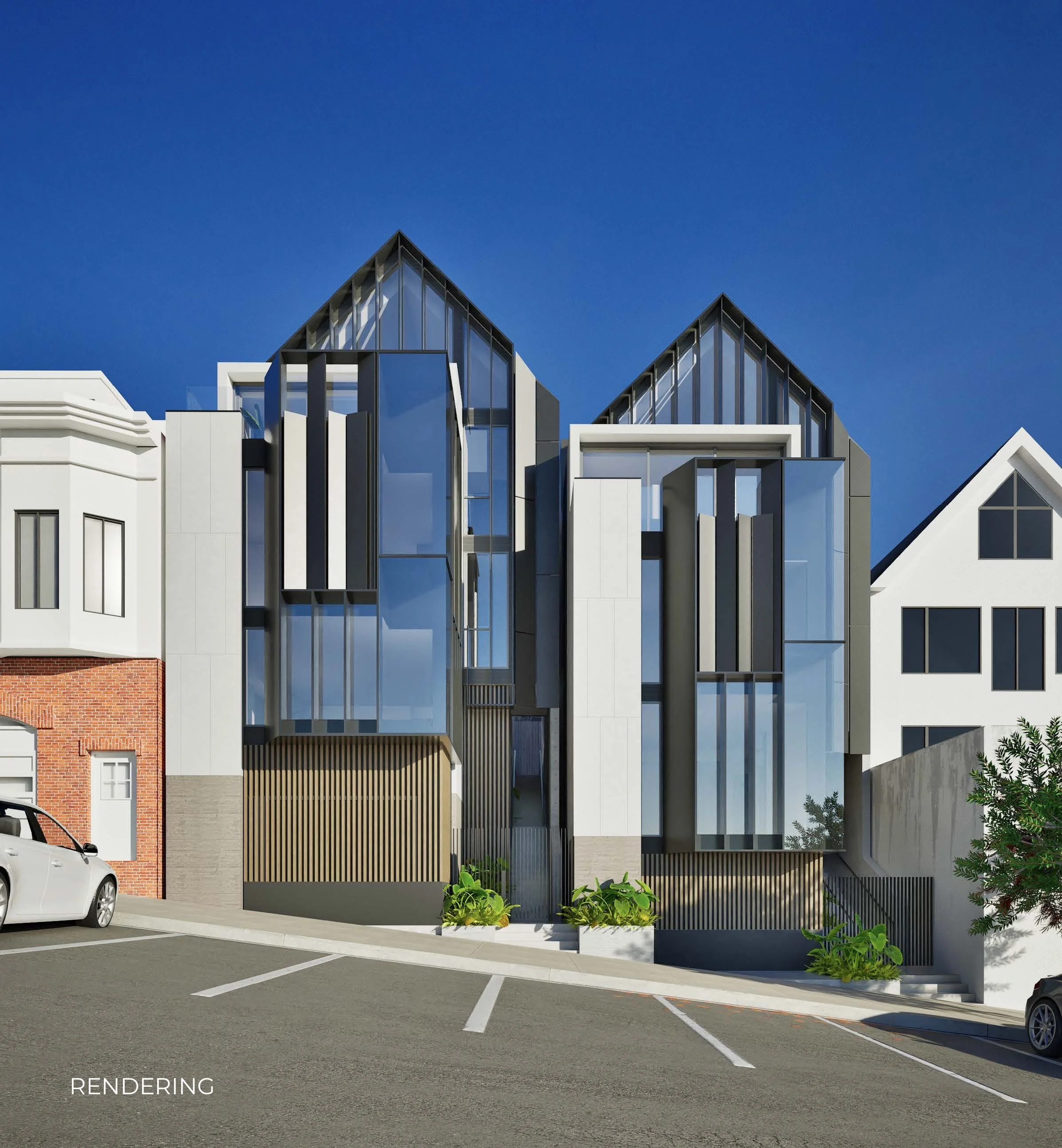 Modern residential building with large glass windows and mixed materials including black metal, white panels, and brick accents. The building is situated next to a parking lot with marked spaces and a white car visible in the foreground. Small plants